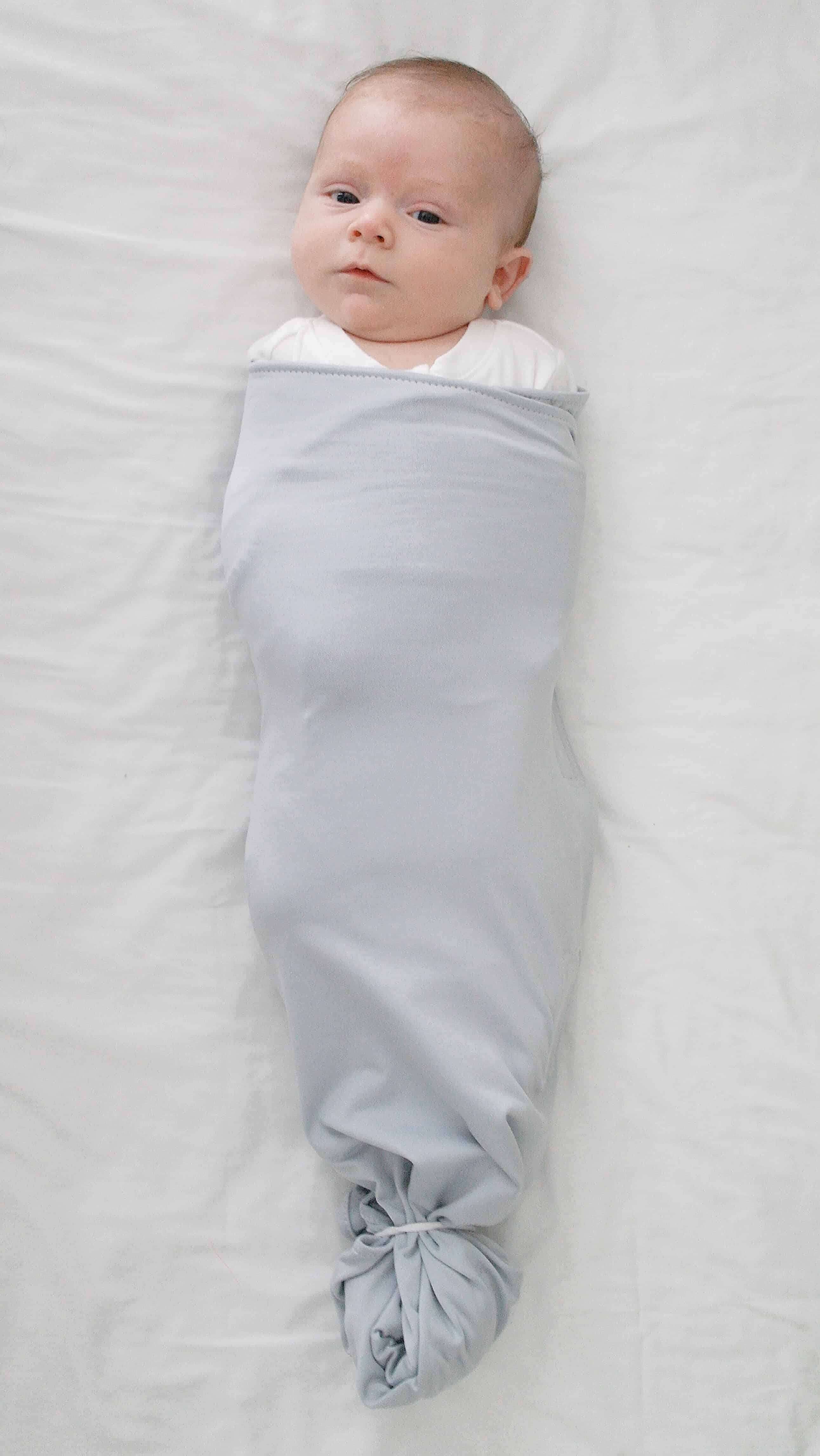 baby in the ollie swaddle on white sheet