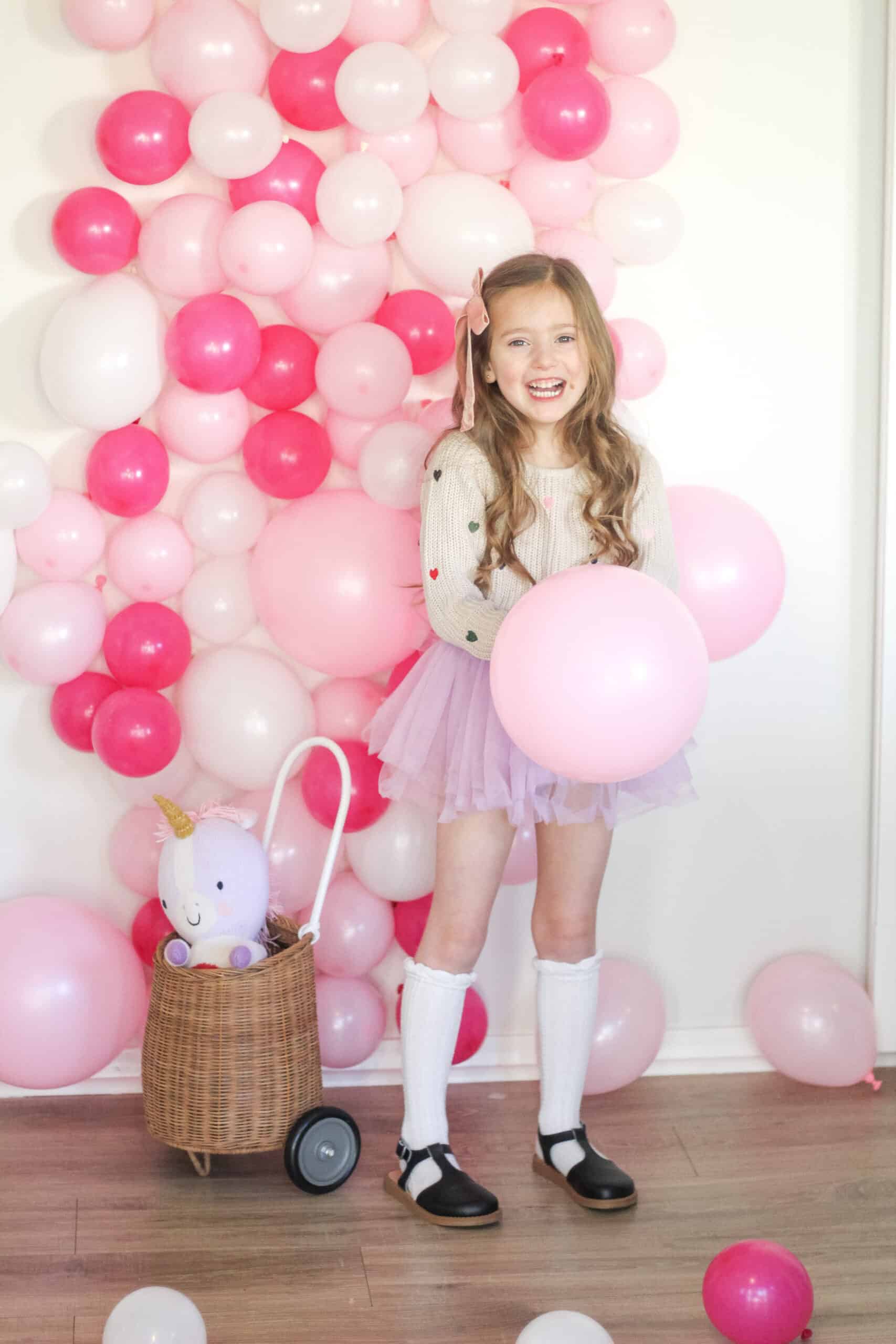 toddler girl in front of pink balloon photo wall