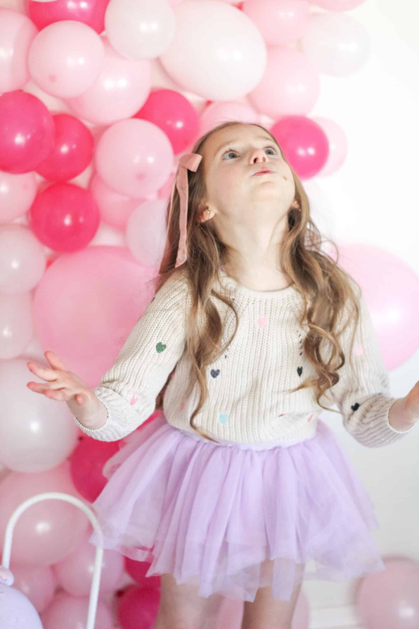 toddler girl in sweater in front of pink balloon wall