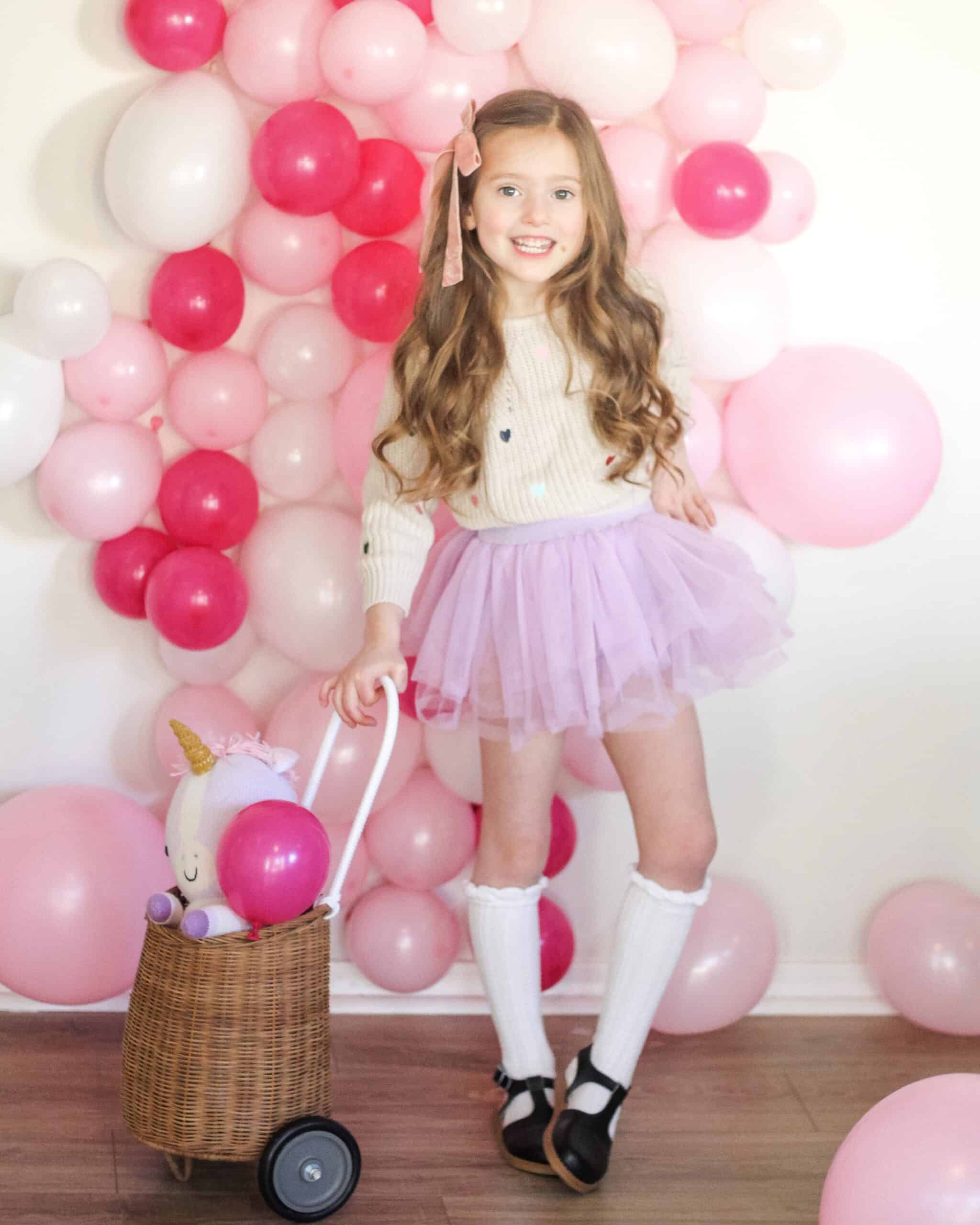toddler girl in front of pink balloon photo wall