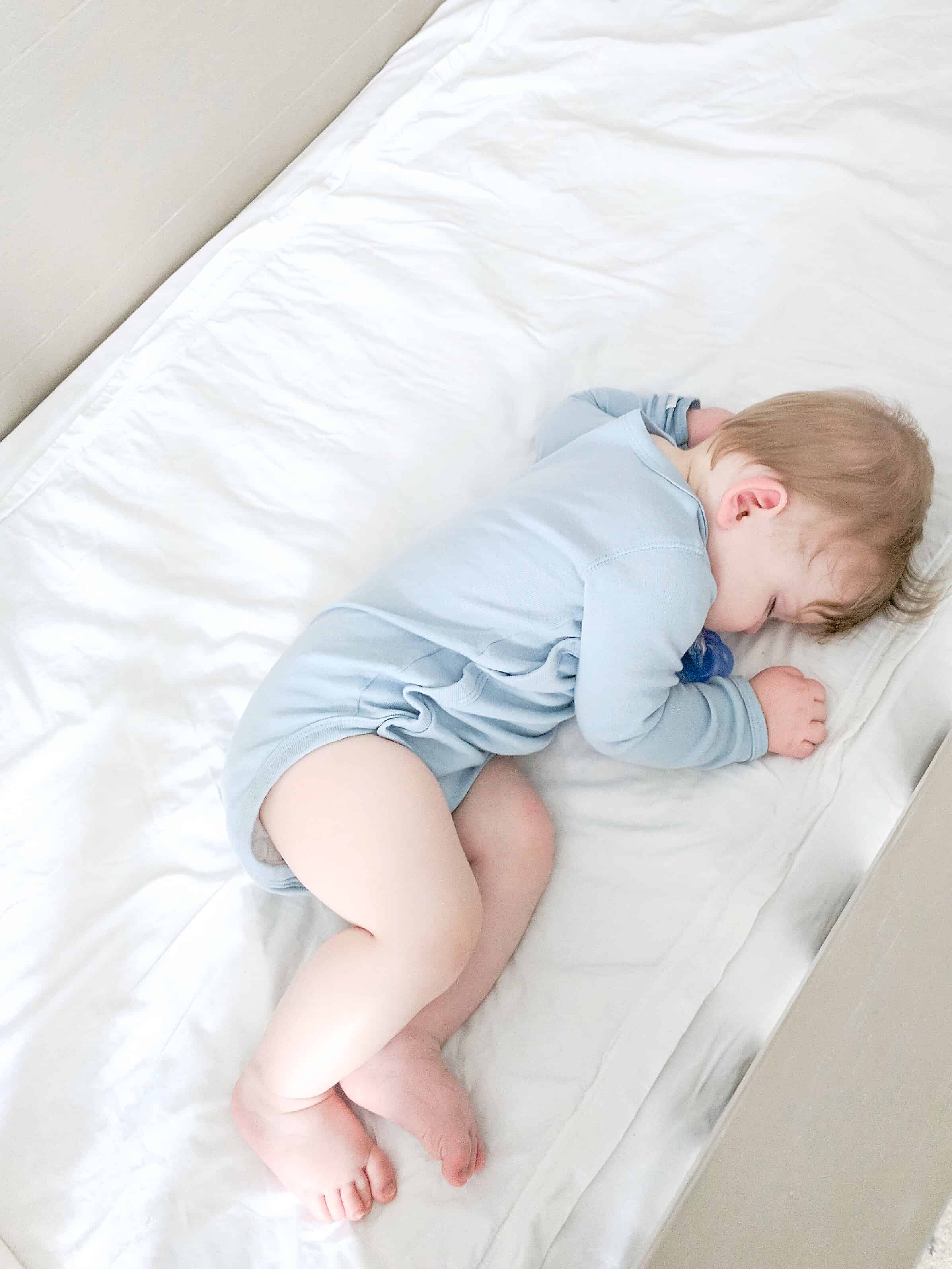 sleeping baby in blue onsie on white sheets