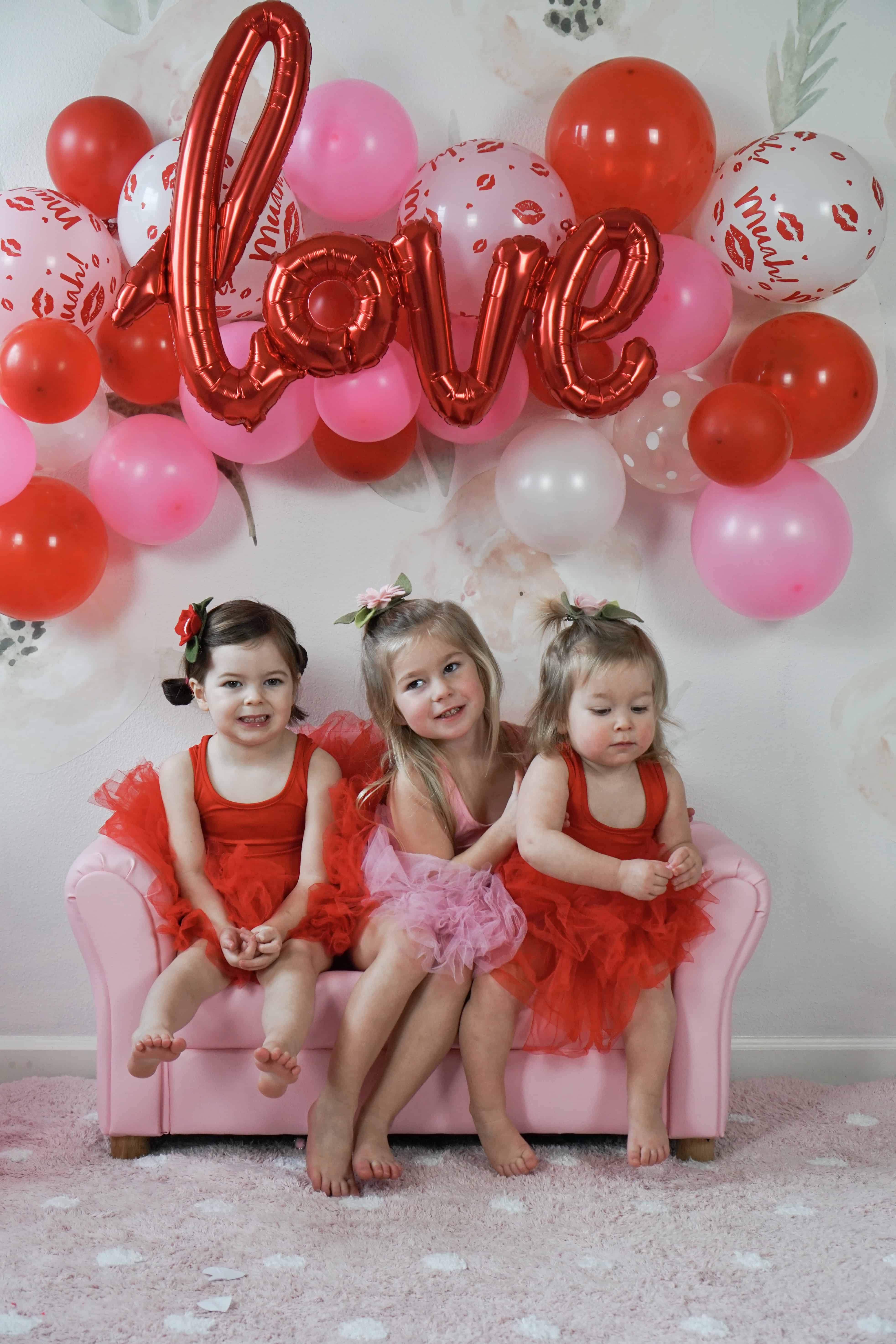 three toddler girls on pink couch in front of balloon wall