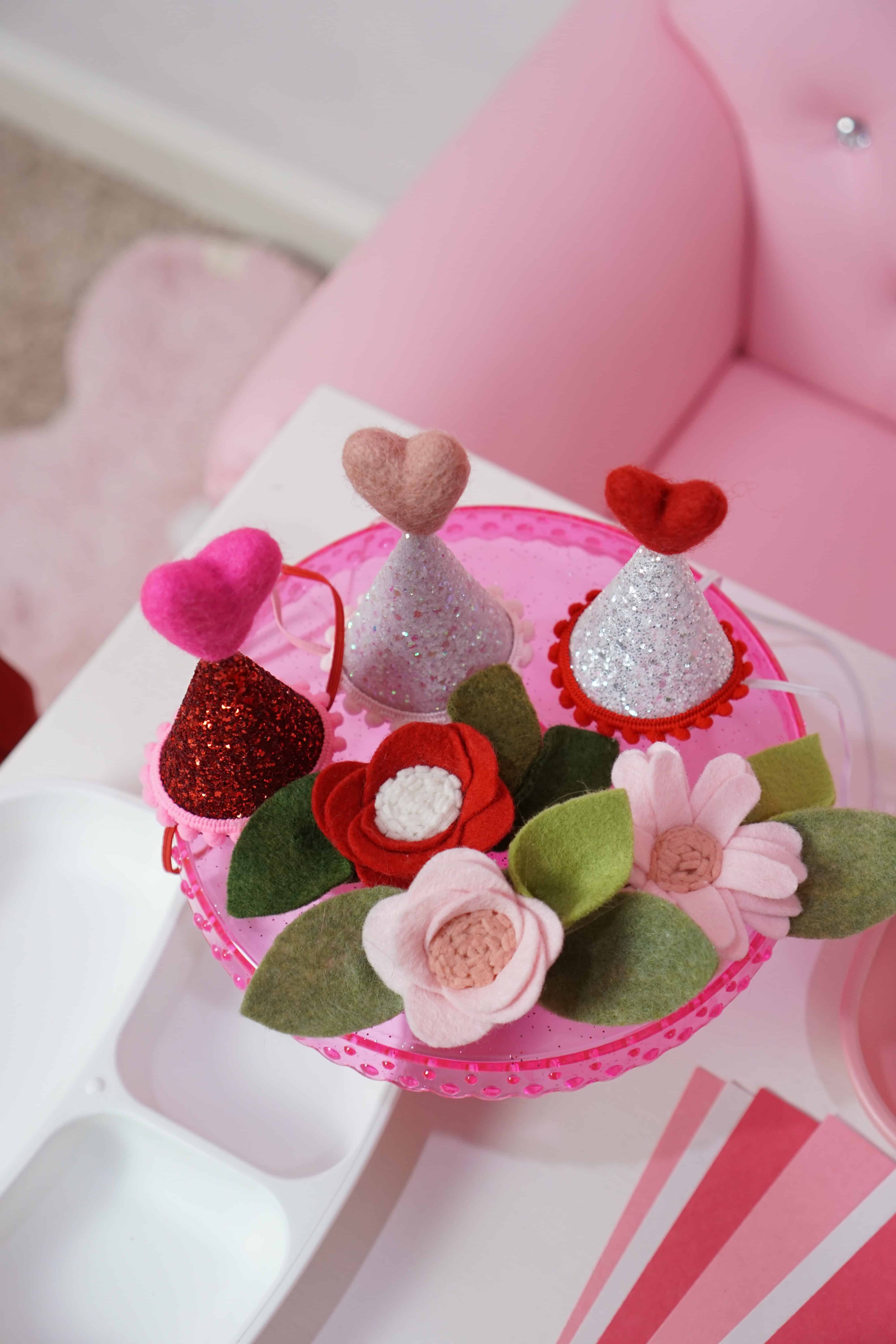 mini heart party hats and flower bows on a pink cake stand