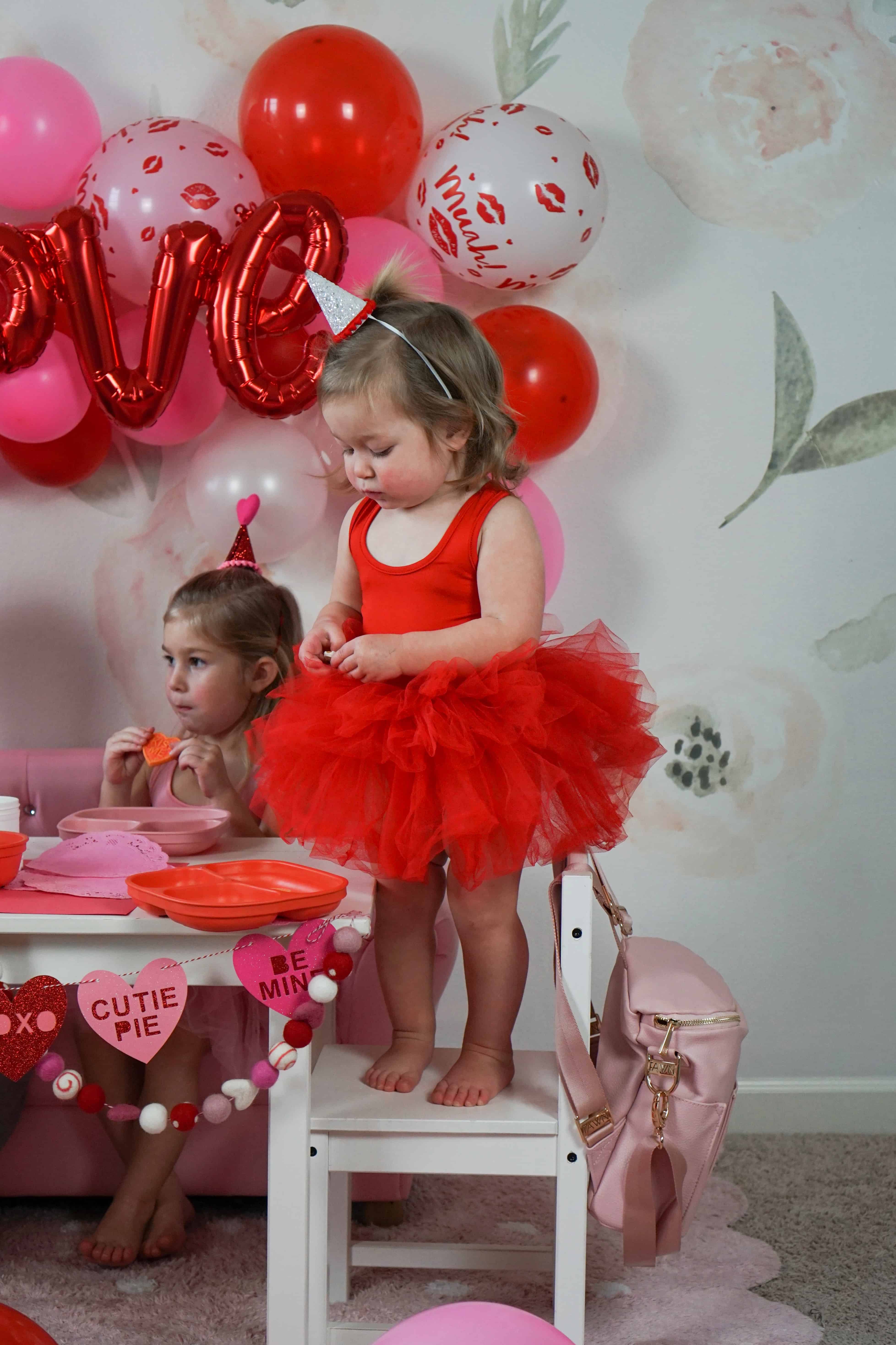 toddler girl in red tutu standing on chair