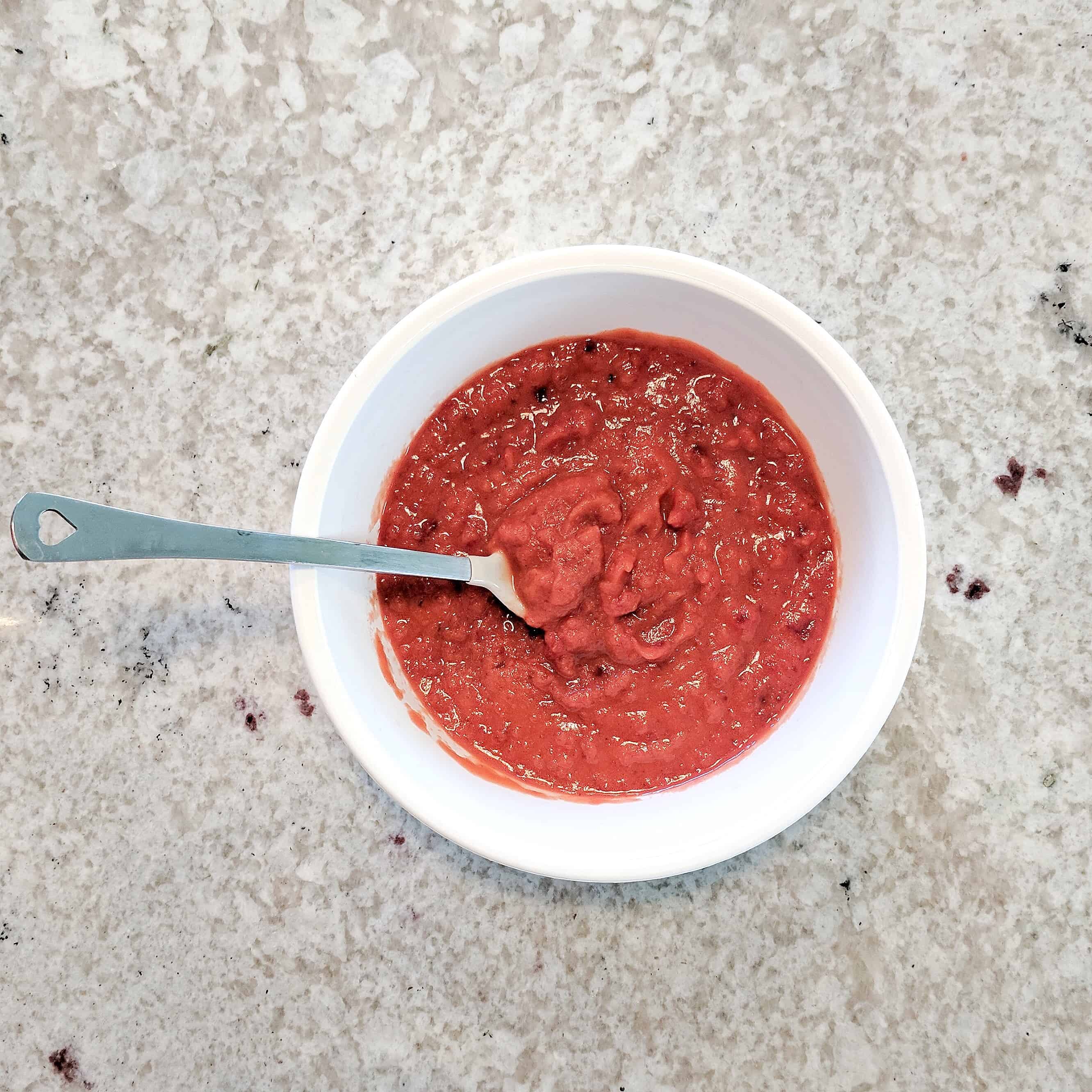 white bowl of red baby food with spoon in it on counter - raised real baby food