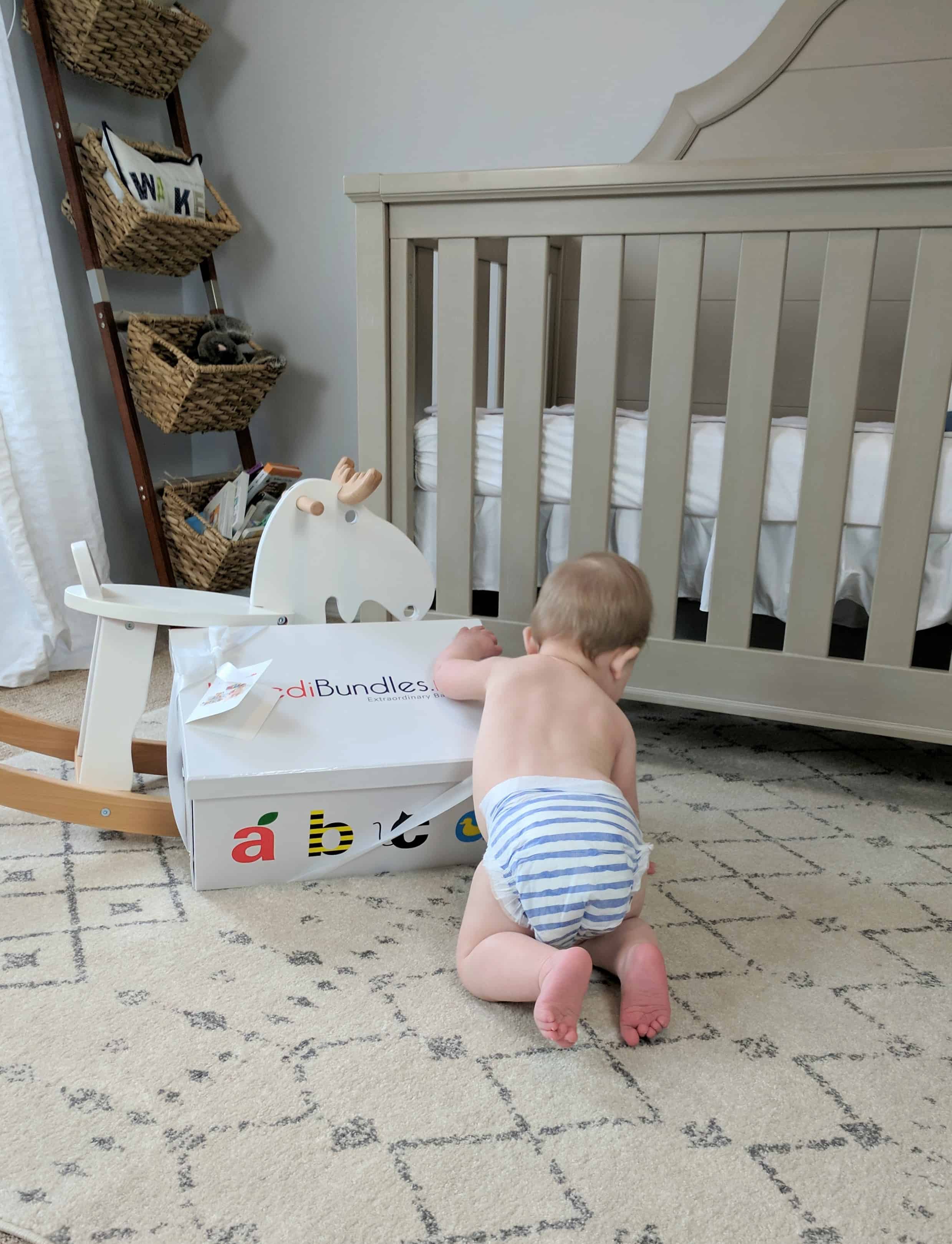 Baby opening box by rocking horse and crib