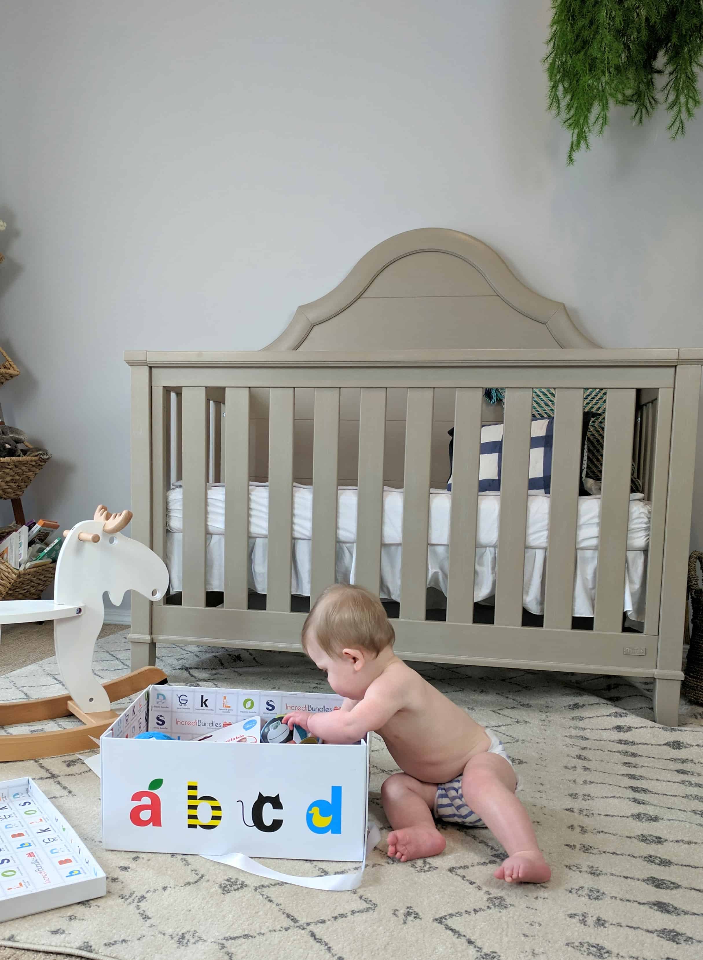 baby digging into box of gifts by rocking horse and crib