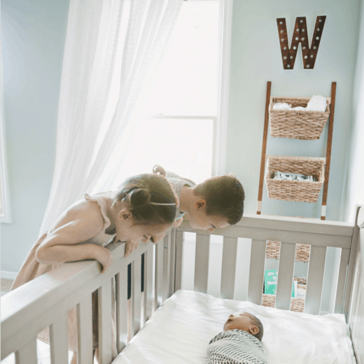 two toddlers looking at baby in a crib