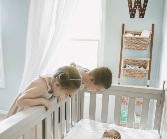two toddlers looking at baby in a crib