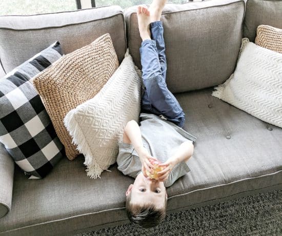 little boy eating apple on grey couch