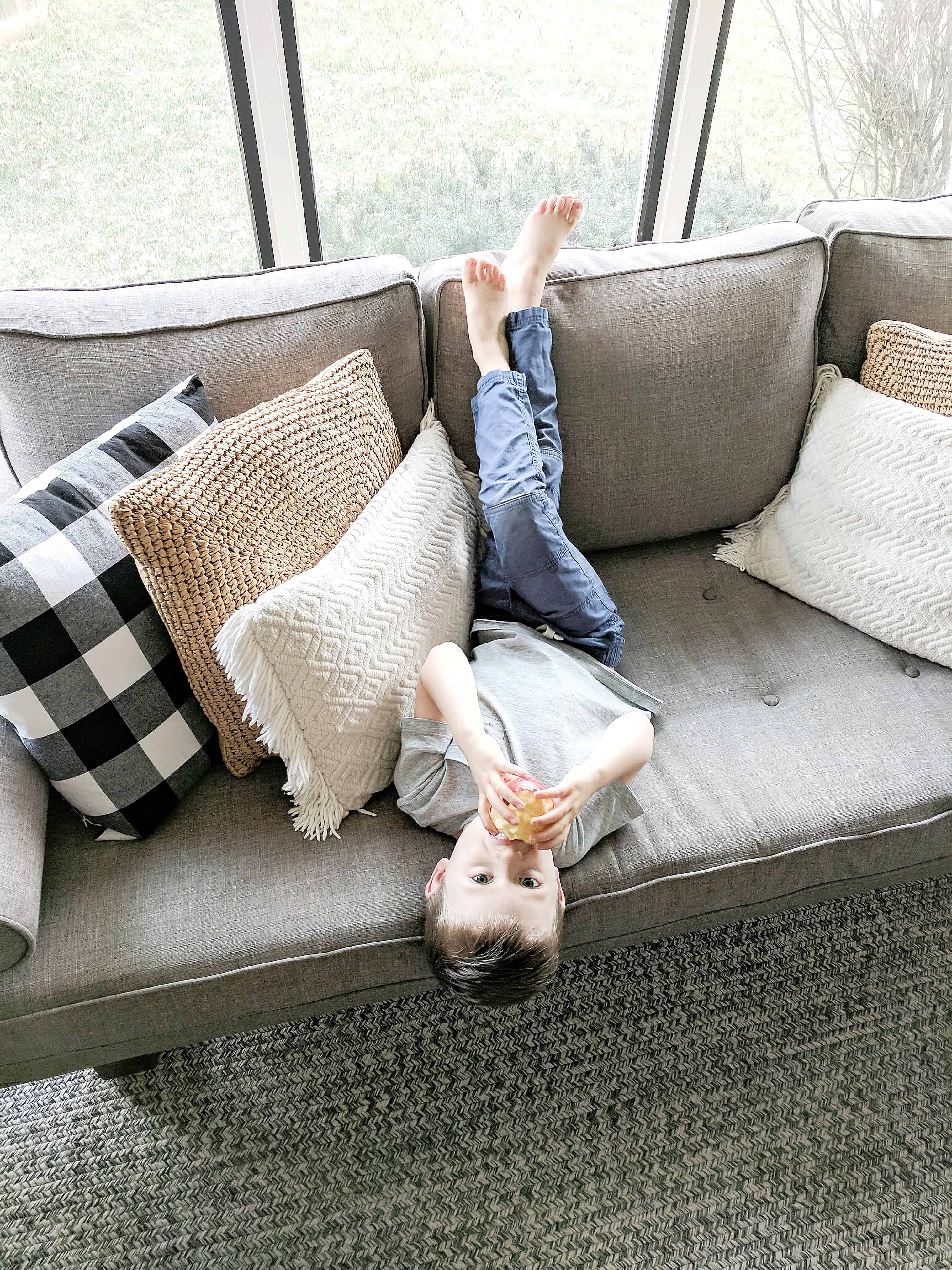 little boy eating apple on grey couch