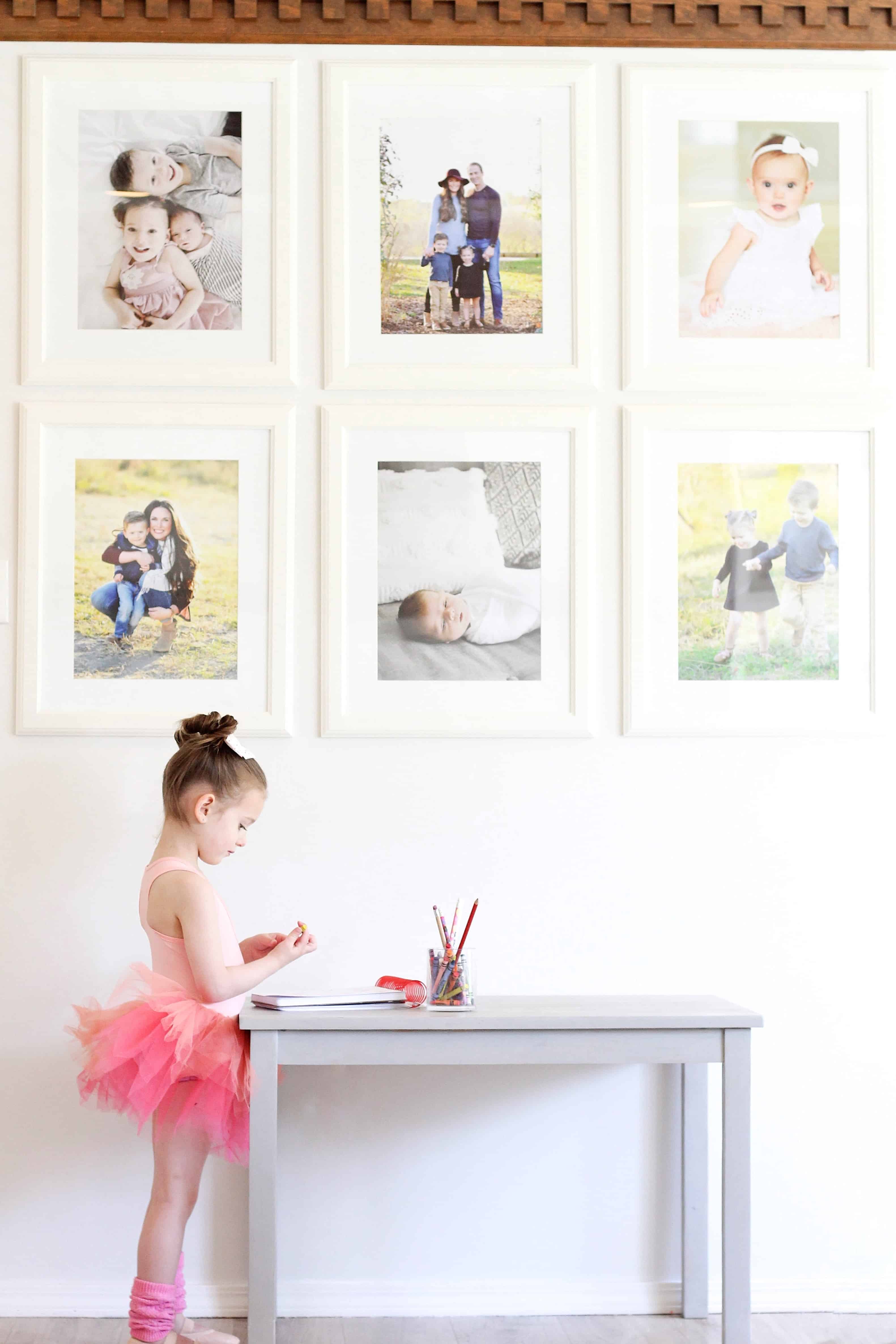 little girl in plum tutu standing by photo wall