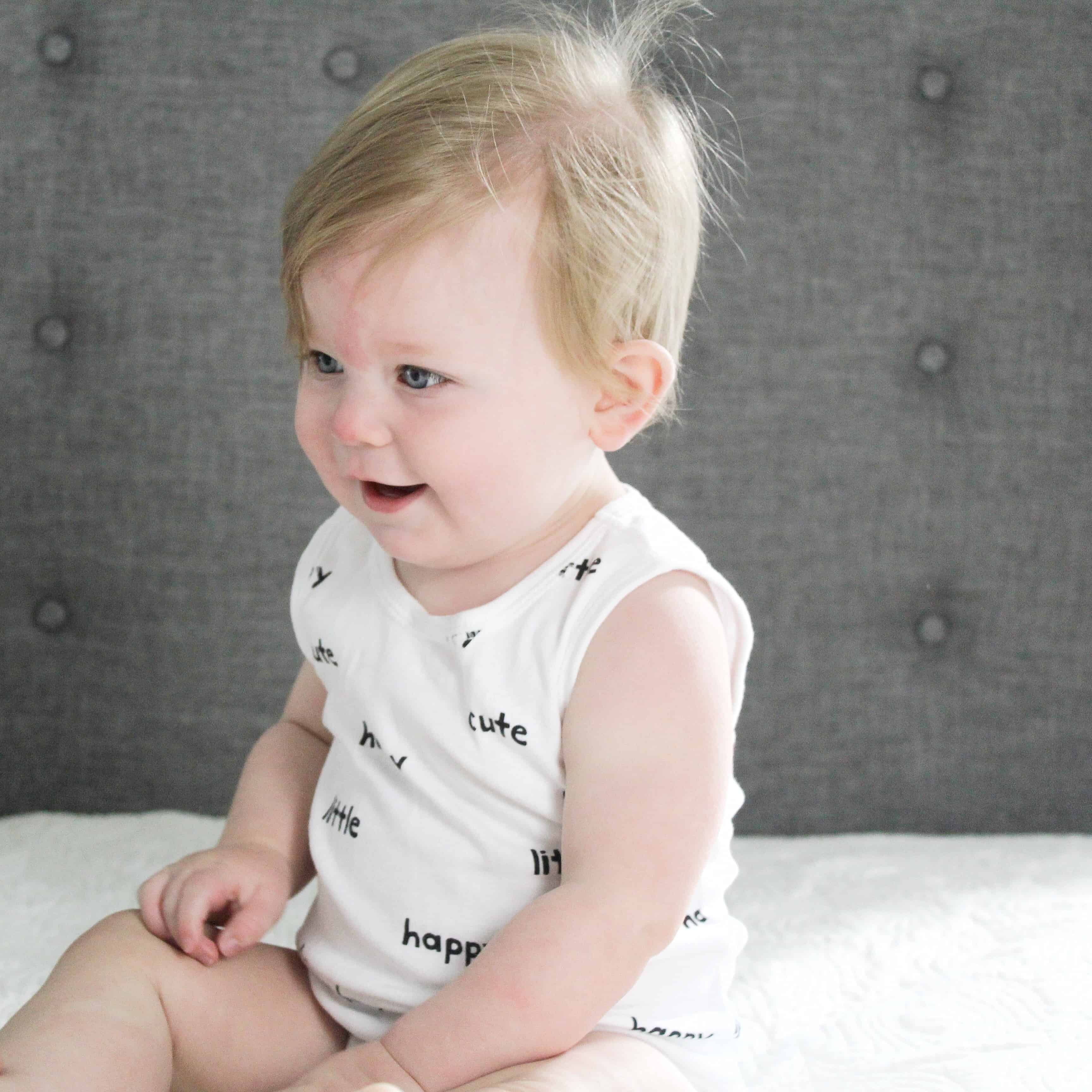 baby sitting on bed in white onsie