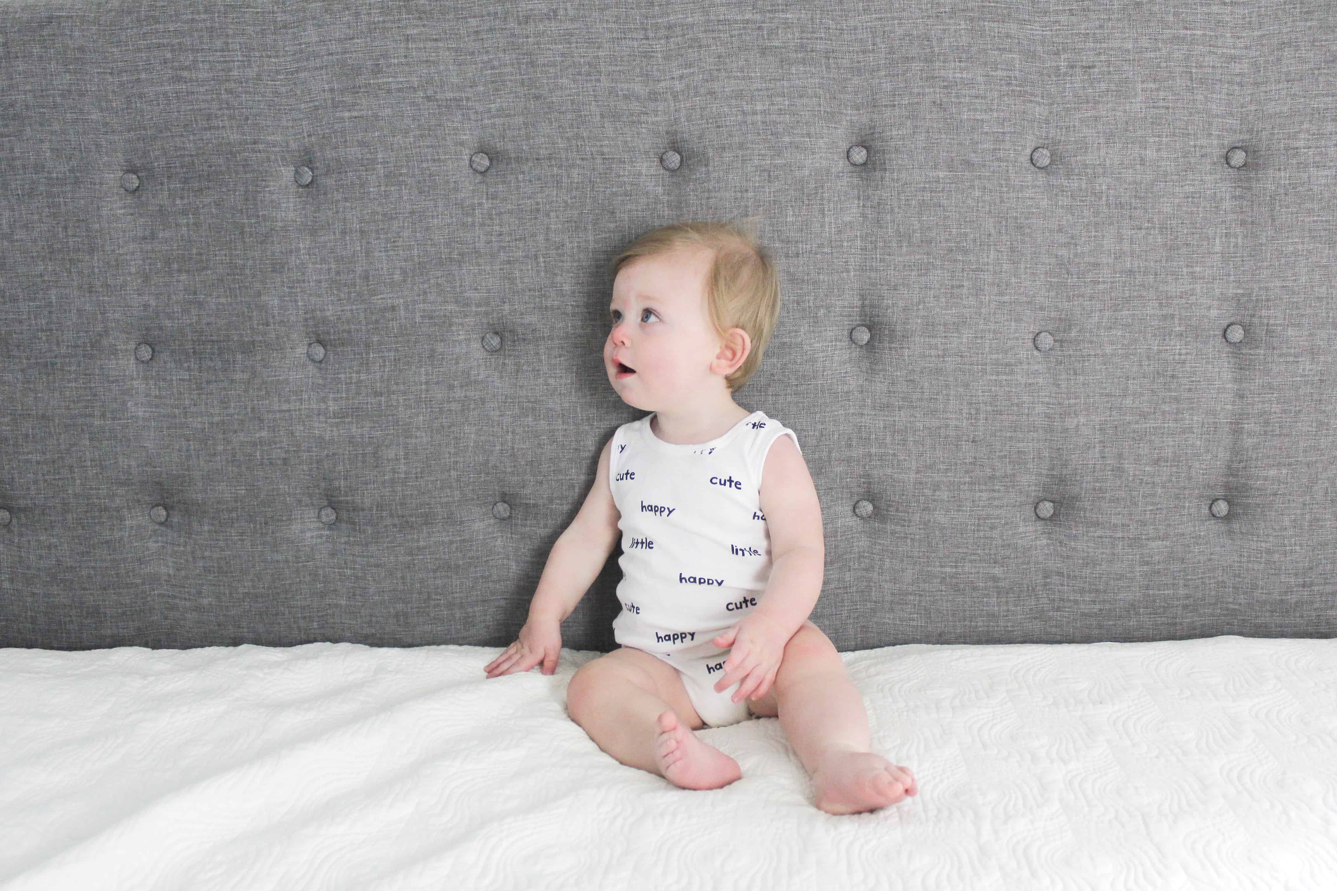 baby in white carters onsie sitting on bed