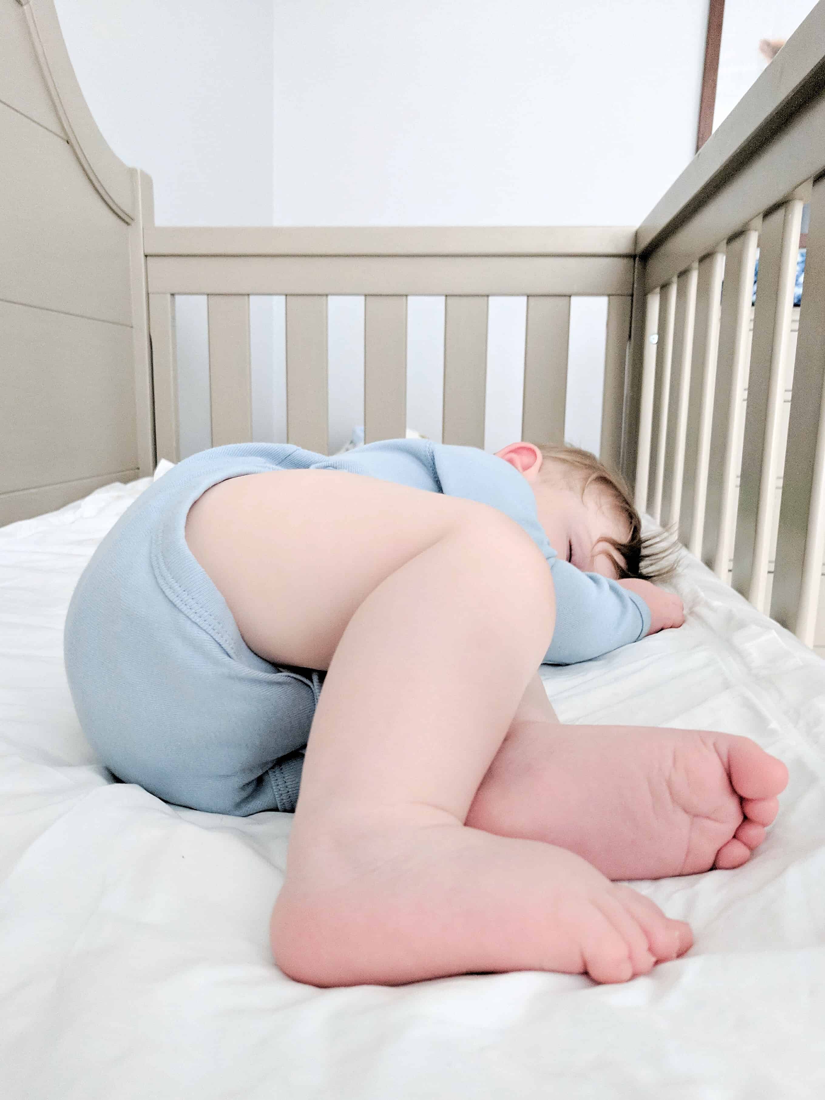 baby sleeping in crib in blue onsie