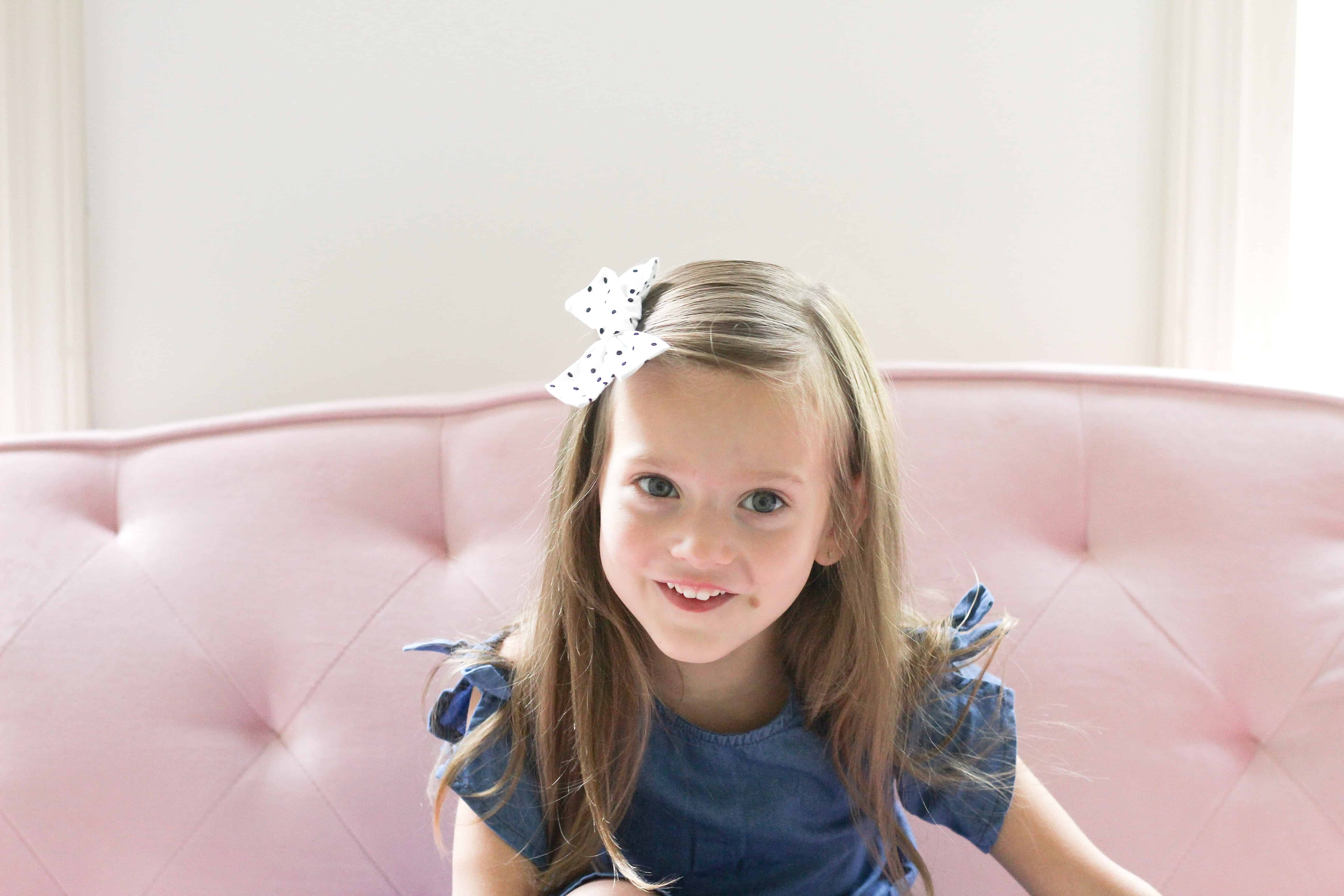 little girl on pink couch in denim dress