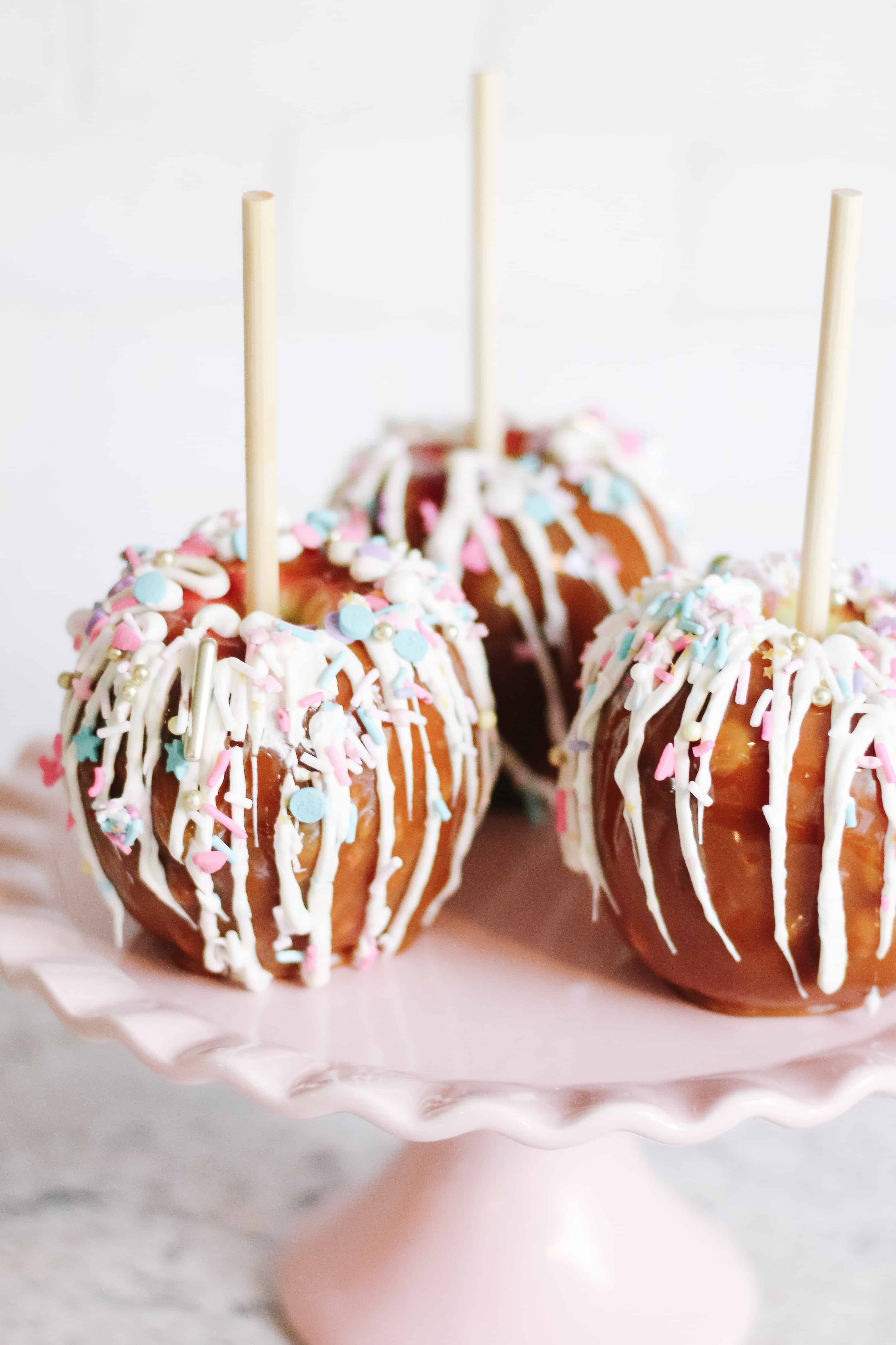 Close up of unicorn caramel apples on pink cake stand