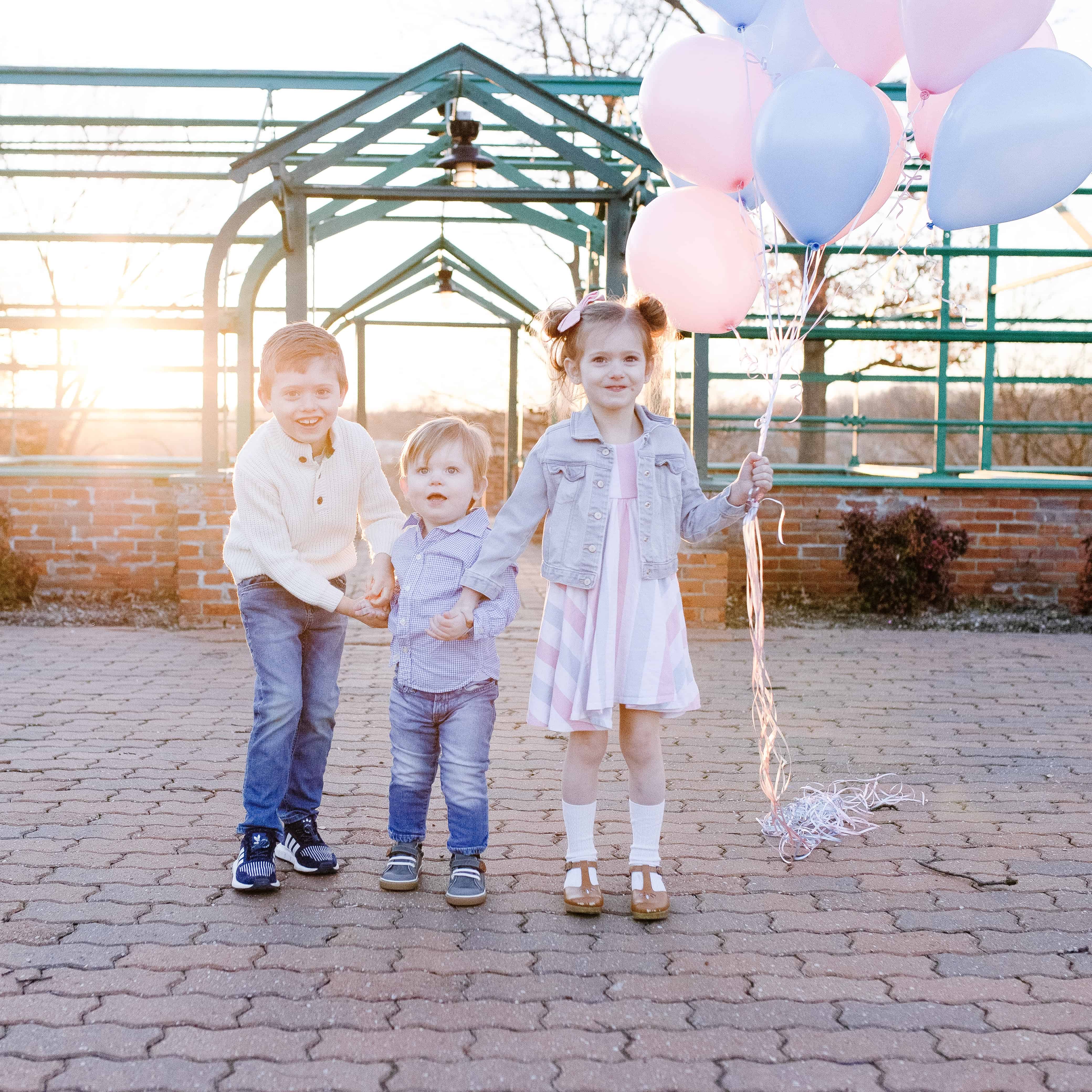 three kids with pink and blue balloons