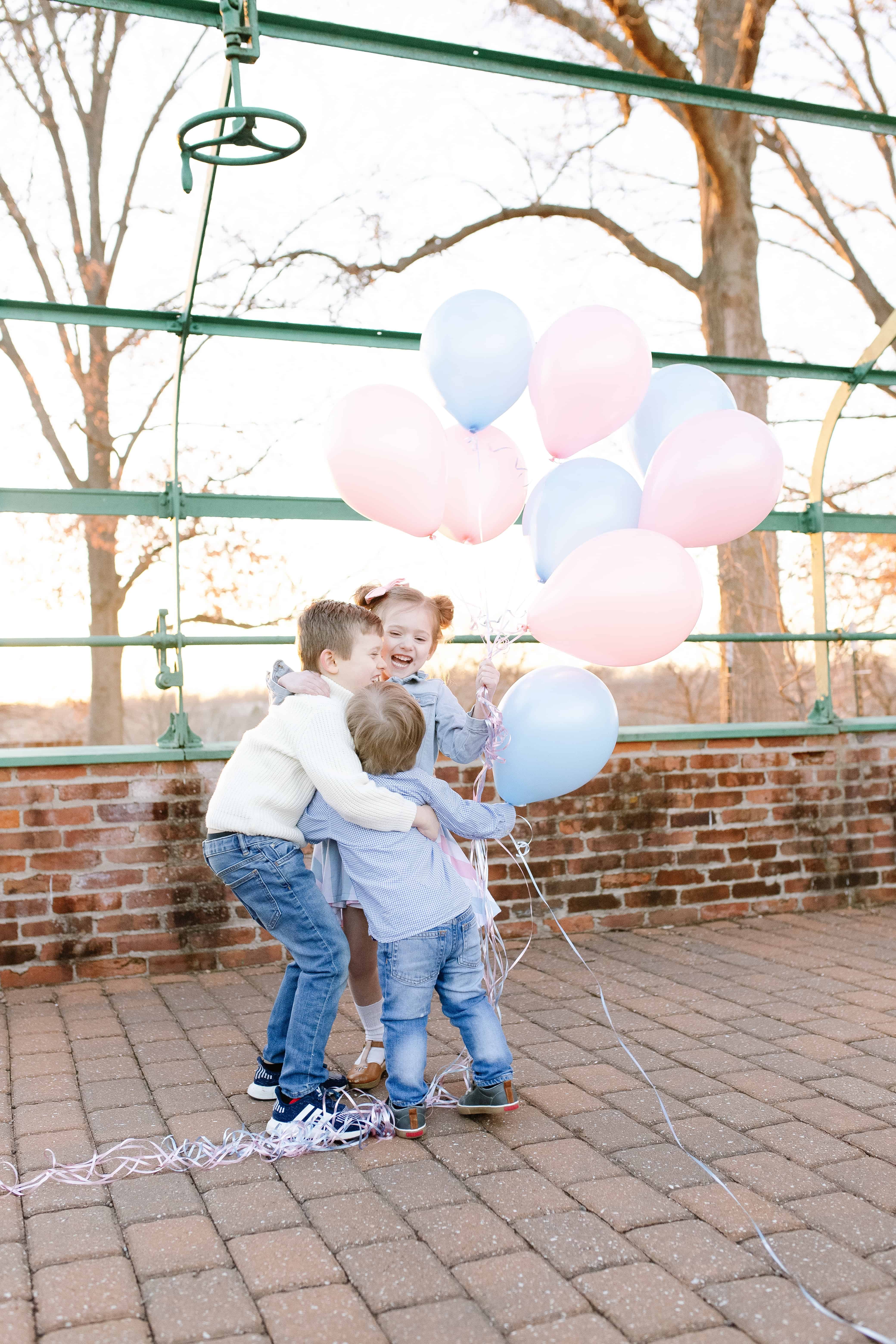 Siblings hugging with pink and blue balloons