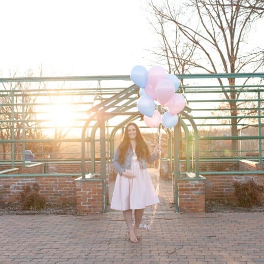 pregnant mom holding pink and blue balloons