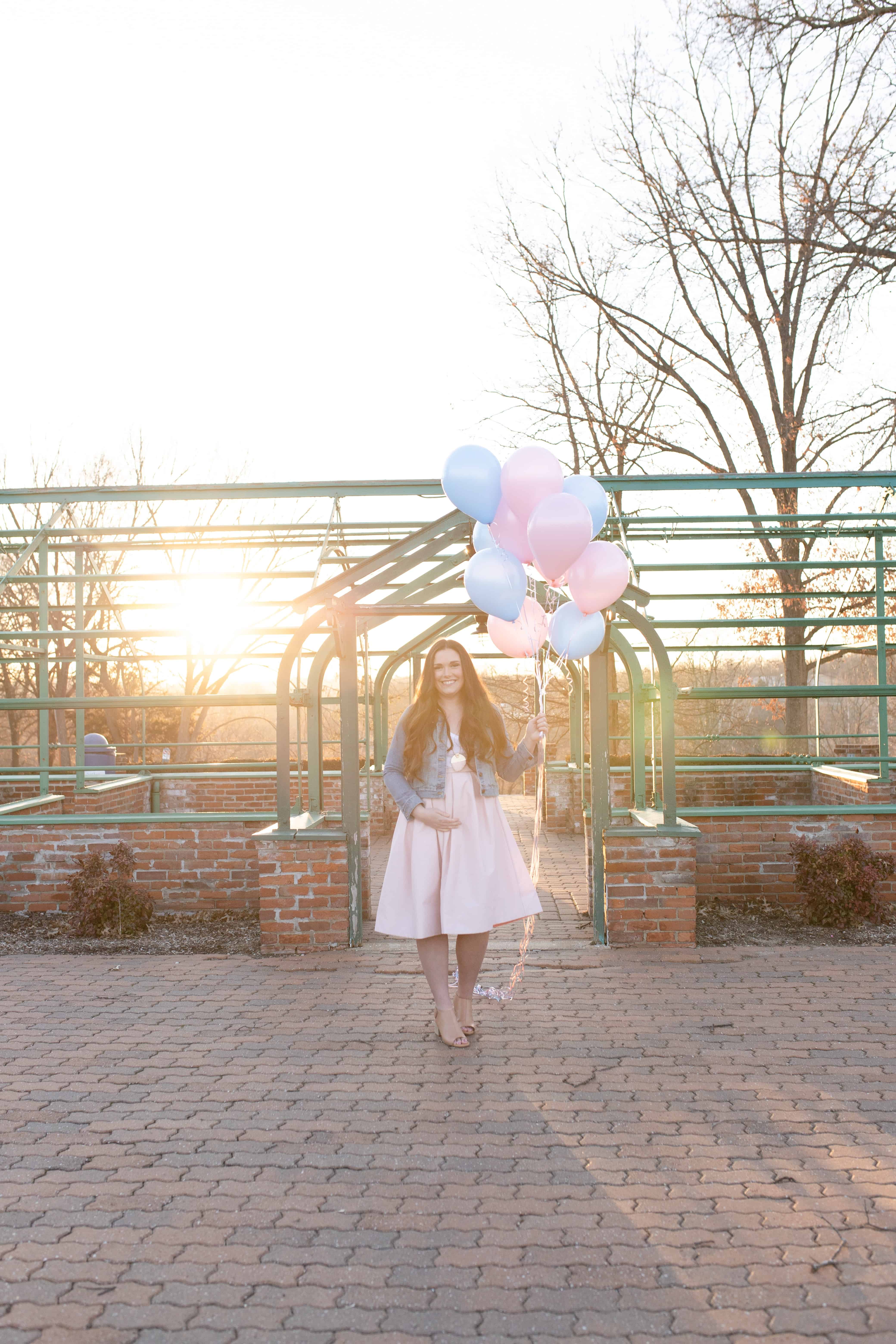 pregnant mom holding pink and blue balloons