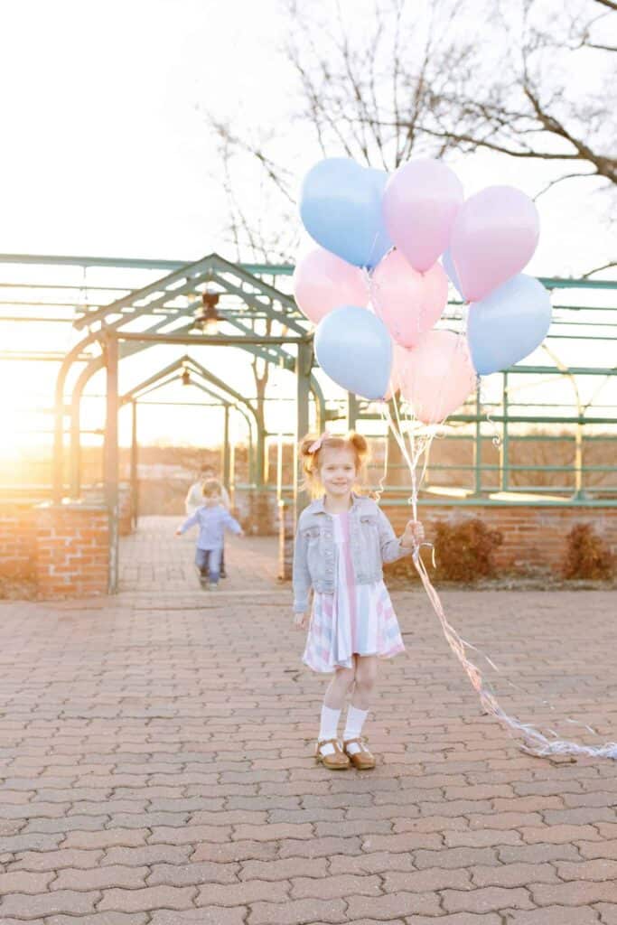 Little girl holding balloons waiting on gender reveal for from sneak peek gender test