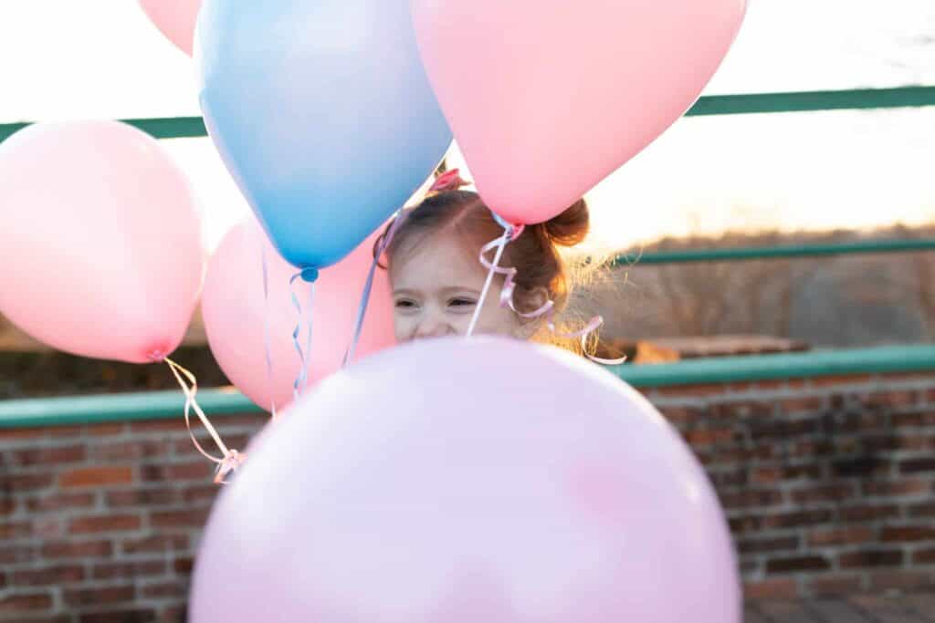 little girl hiding in balloons waiting for sneak peek test gender reveal