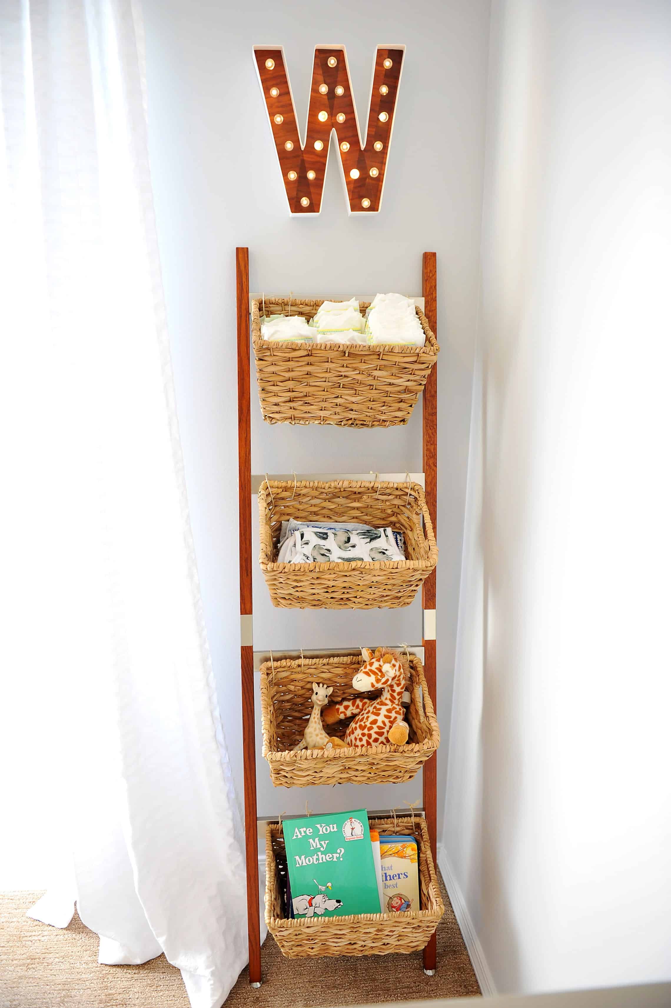 Wicker basket storage ladder with nursery items and hanging W over it