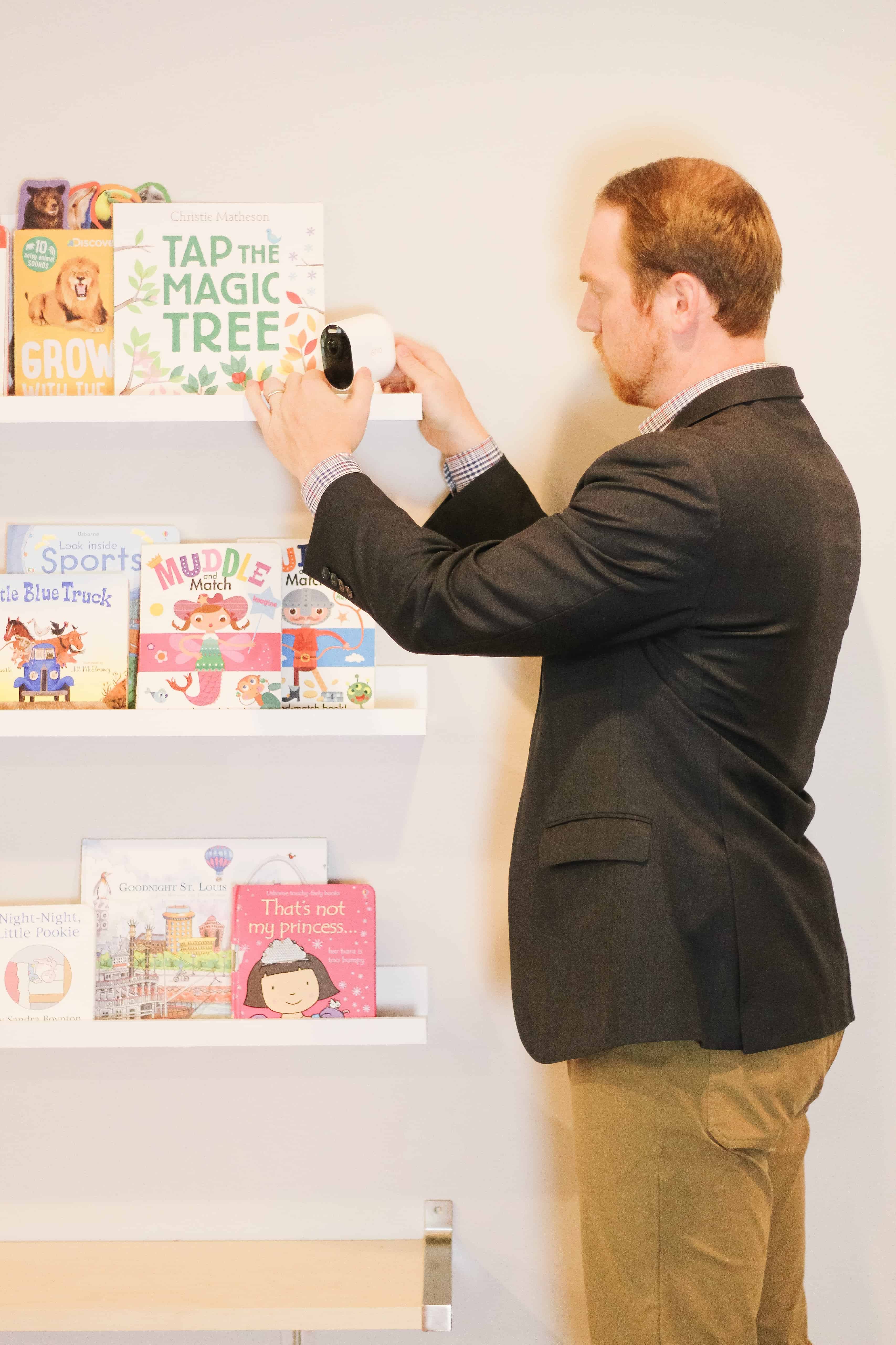 man installing Arlo Ultra monitor on bookshelves