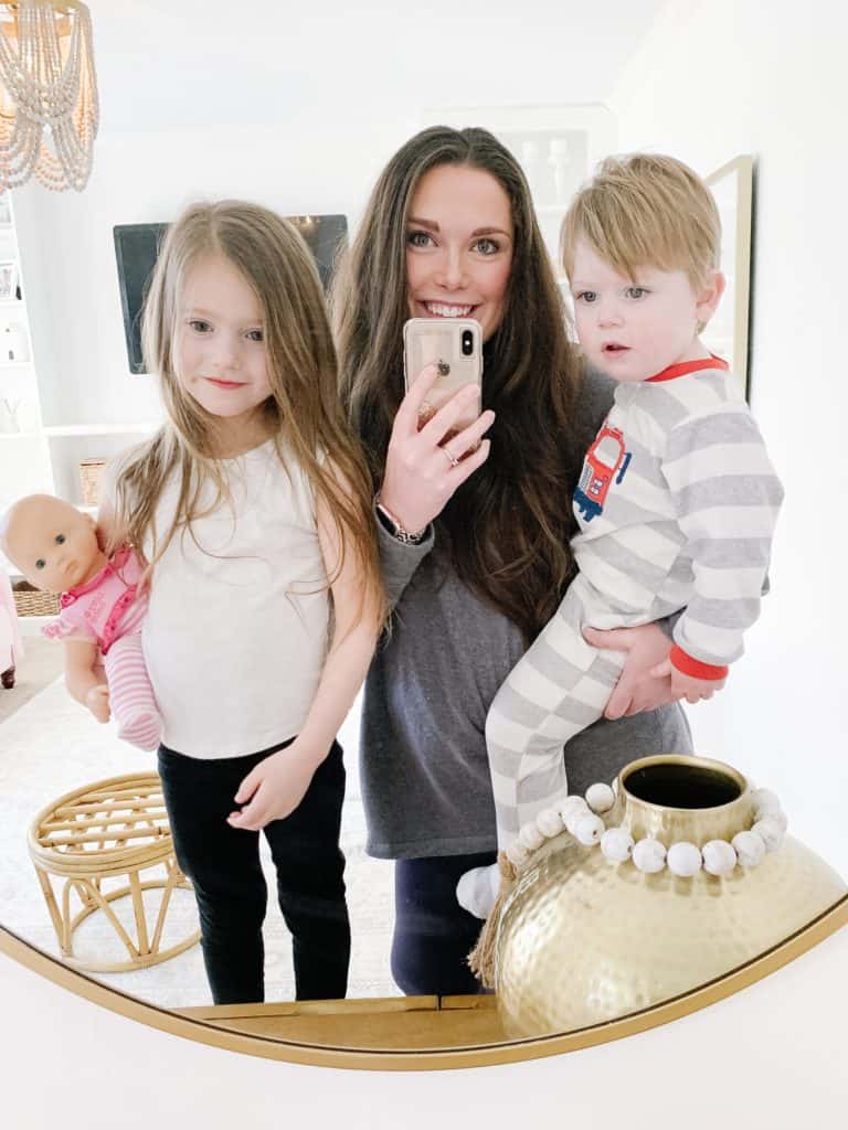 mom holding two toddlers looking in gold round mirror