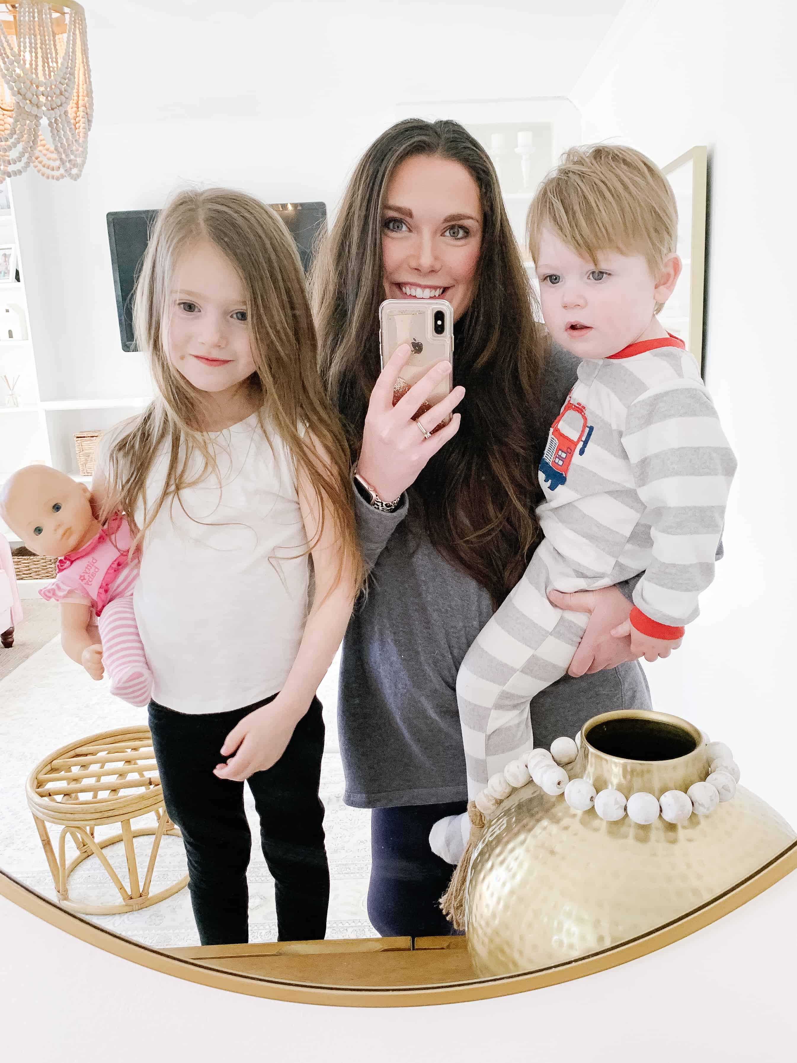 mom holding two toddlers looking in gold round mirror 