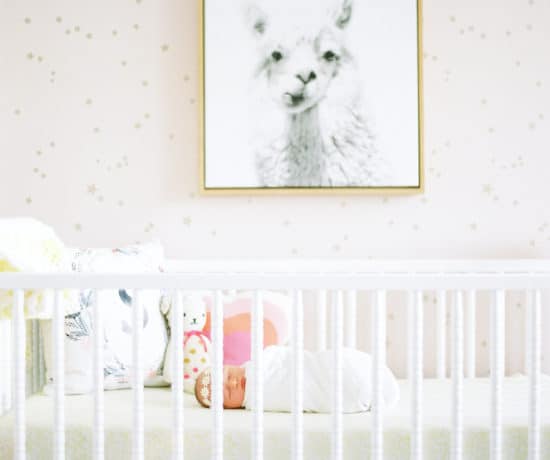 white crib in front of pink and gold star wallpaper with llama photo over crib