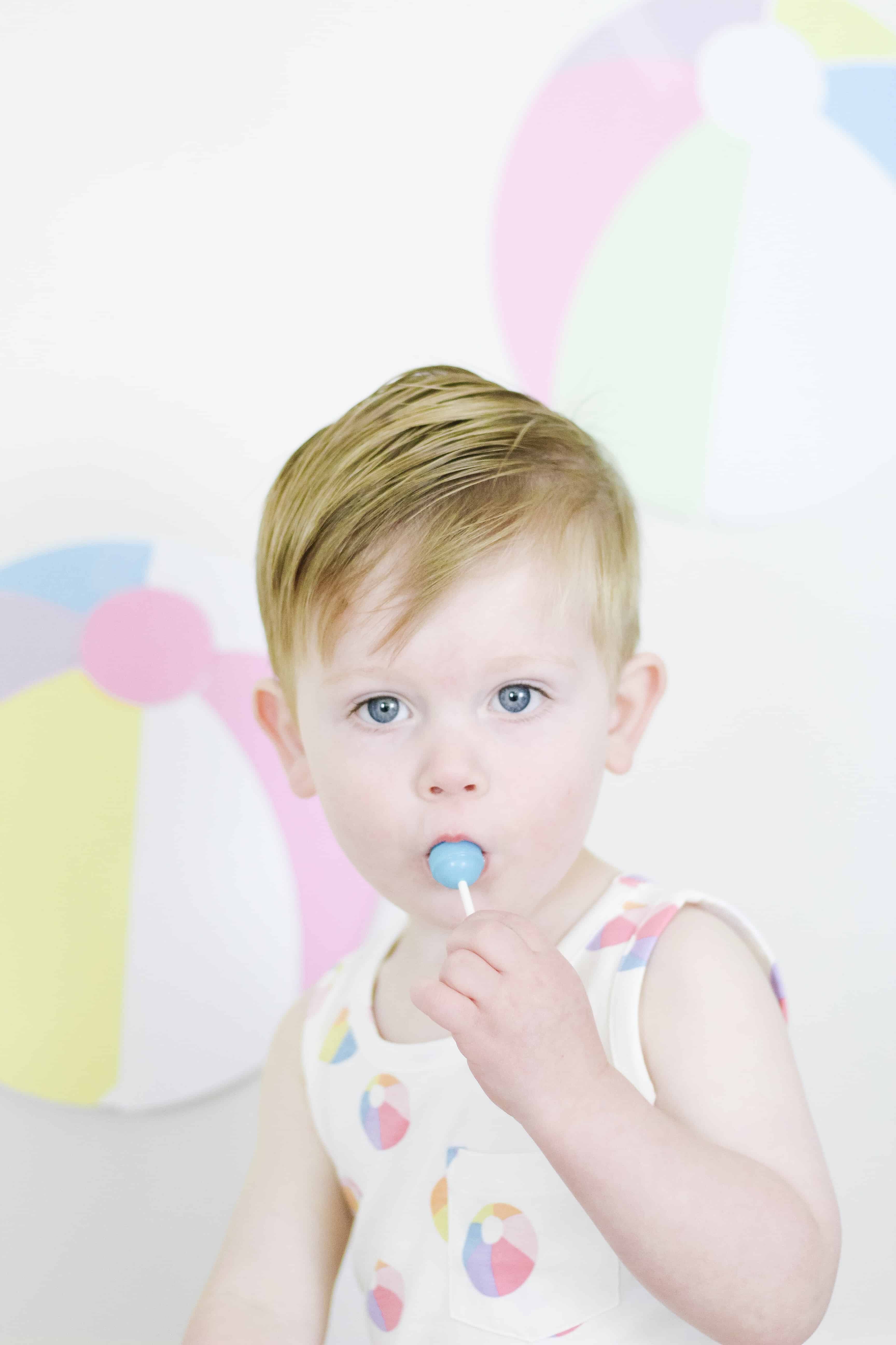 toddler boy in beach ball outfit eating sucker