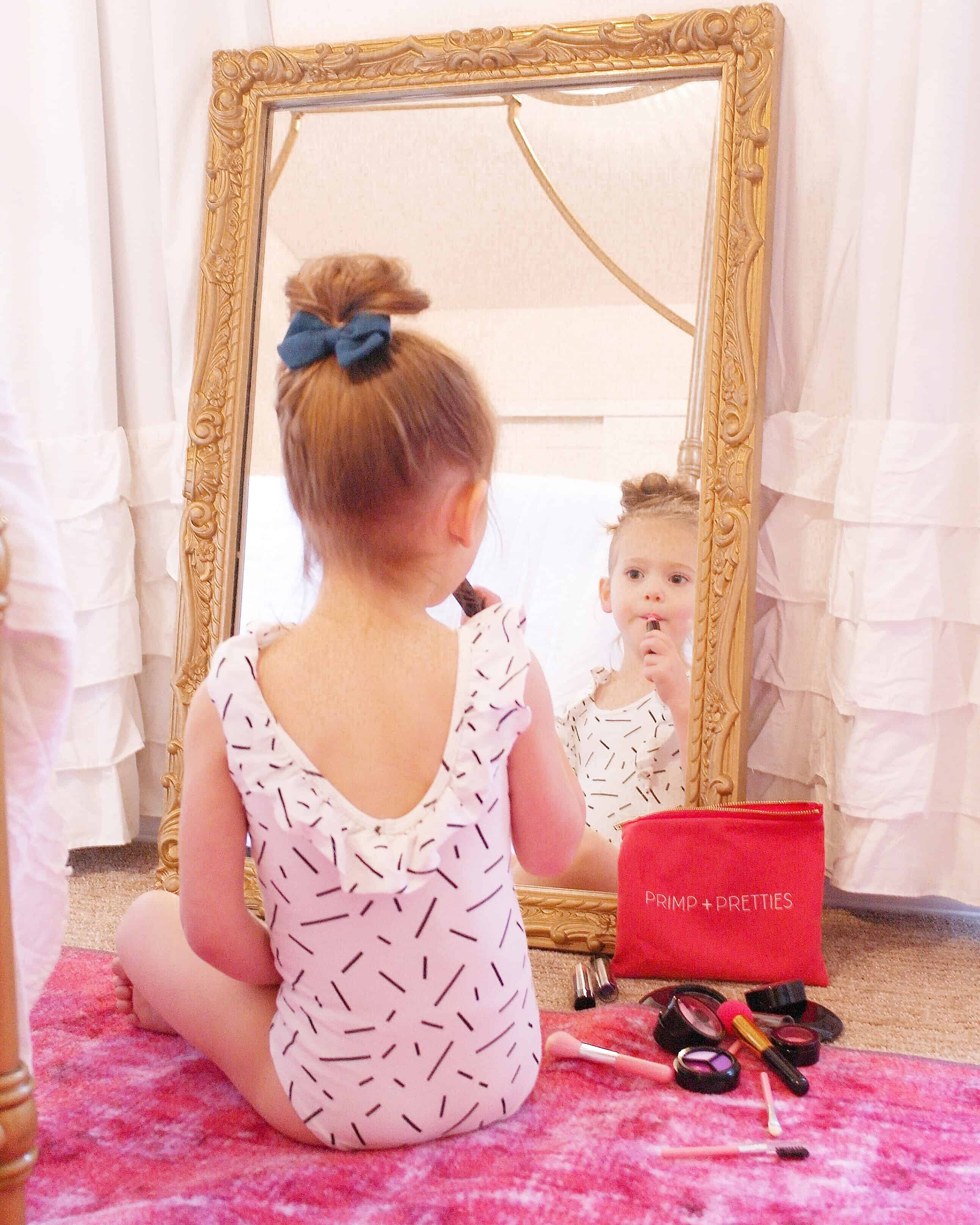 toddler girl putting on pretend makeup in gold mirror