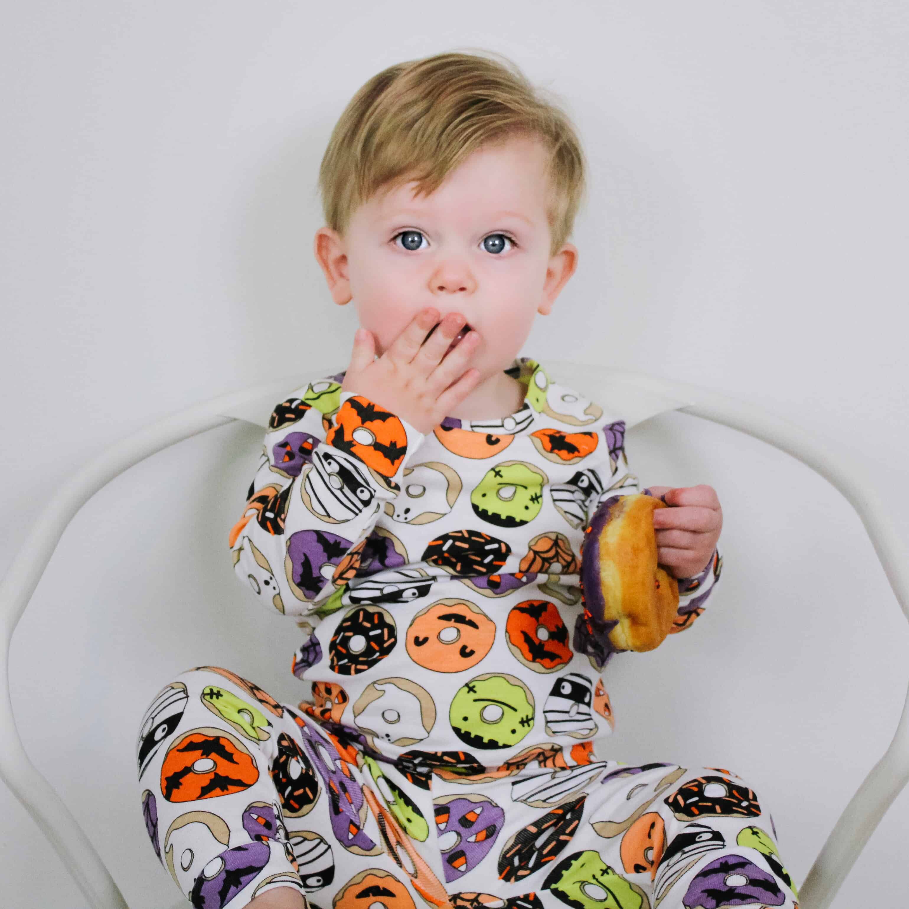 Little boy eating donut in donut halloween pajamas