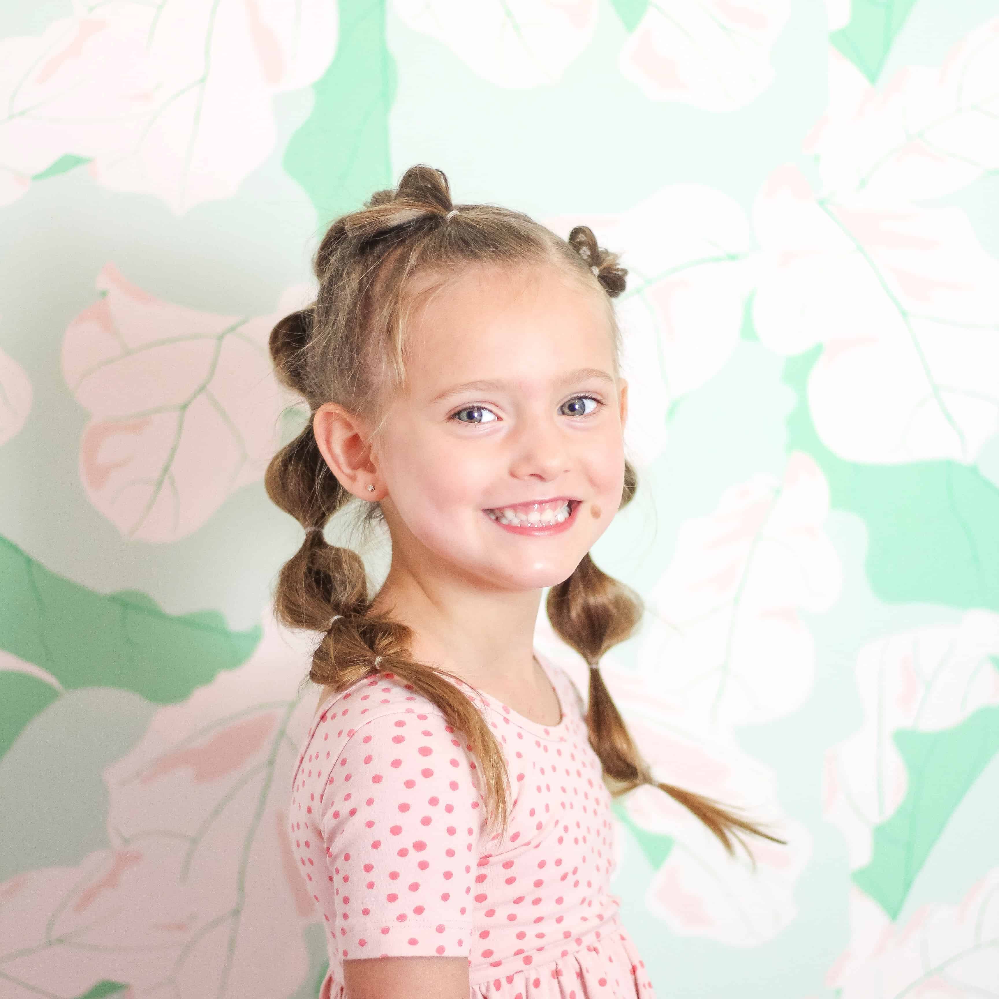 Little girl with bubble braid hair against green floral wall