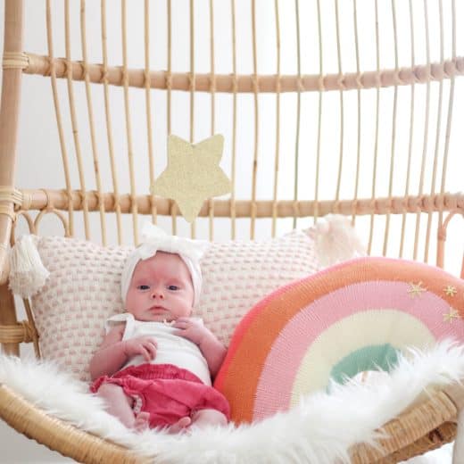 baby girl in Serena and lily hanging chair with rainbow pillow