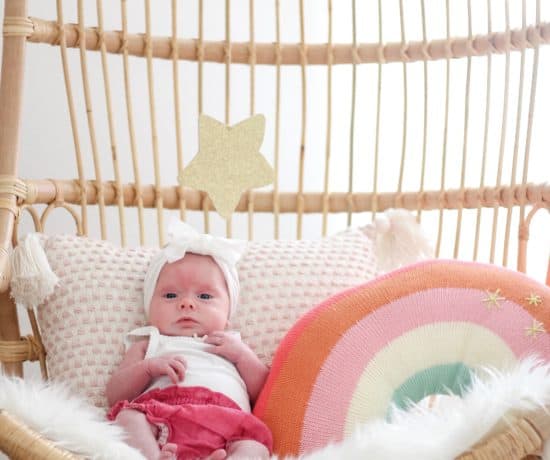 baby girl in Serena and lily hanging chair with rainbow pillow