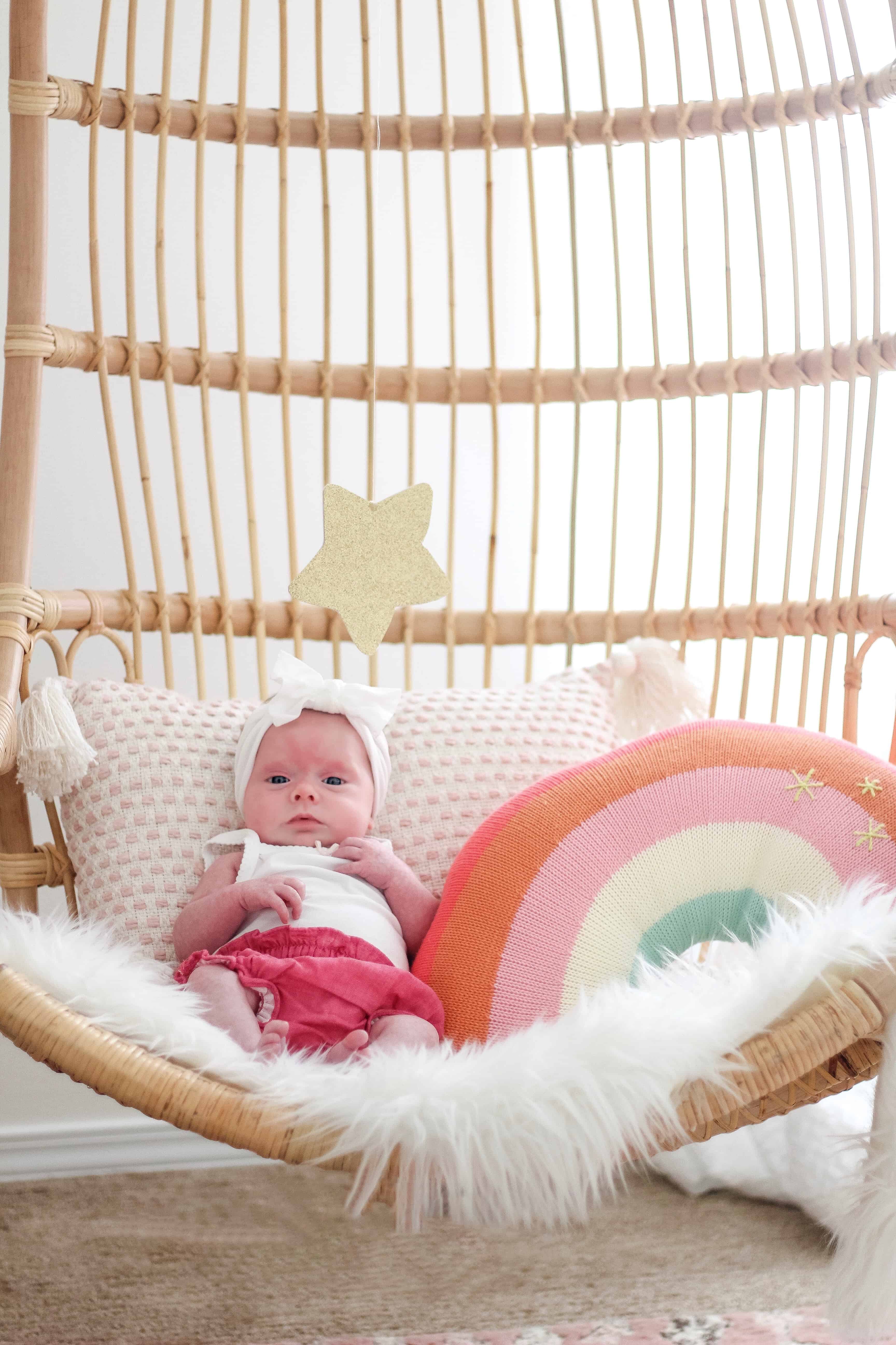 baby girl in Serena and lily hanging chair with rainbow pillow