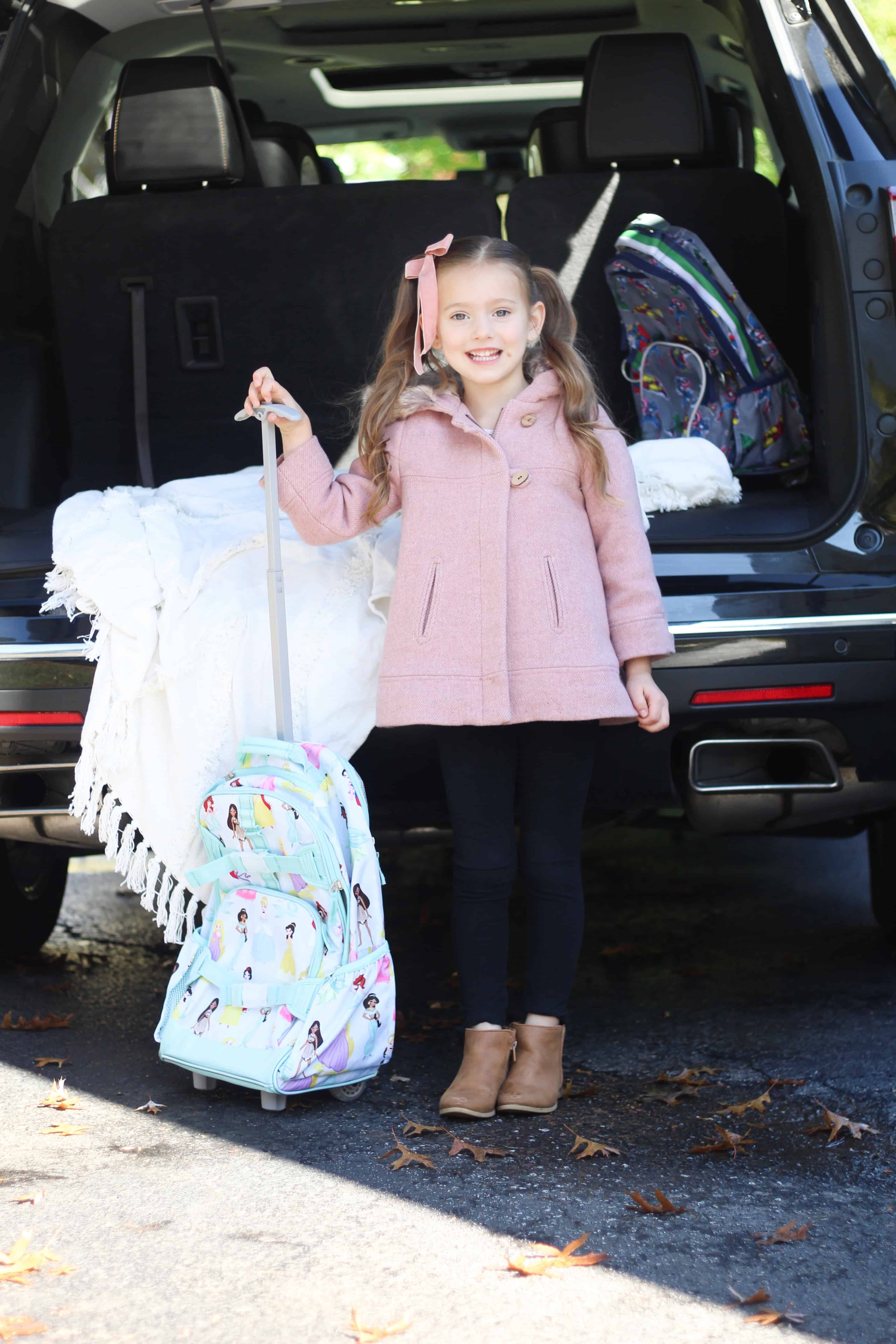 Little girl with suitcase by car