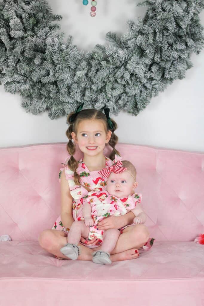 sisters on pink couch in pink Santa dresses