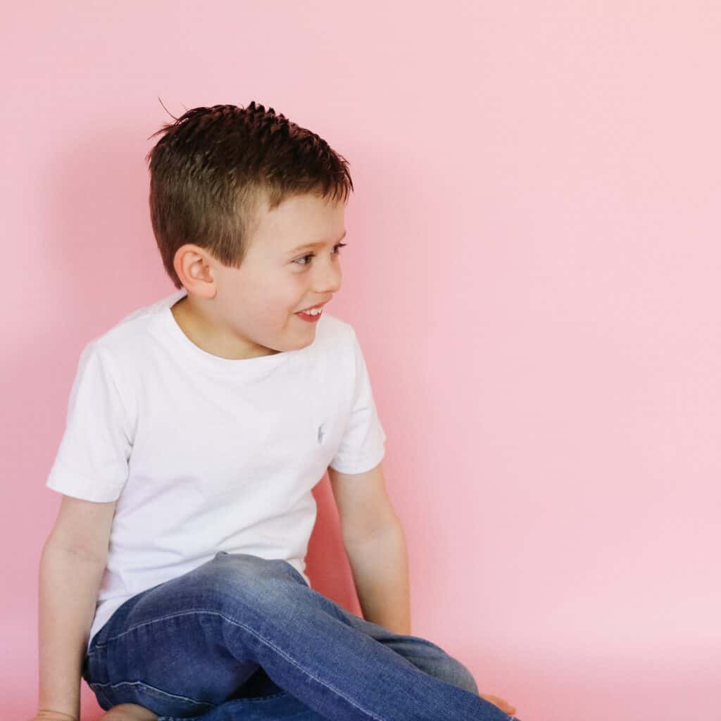 little boy in white against pink backdrop 