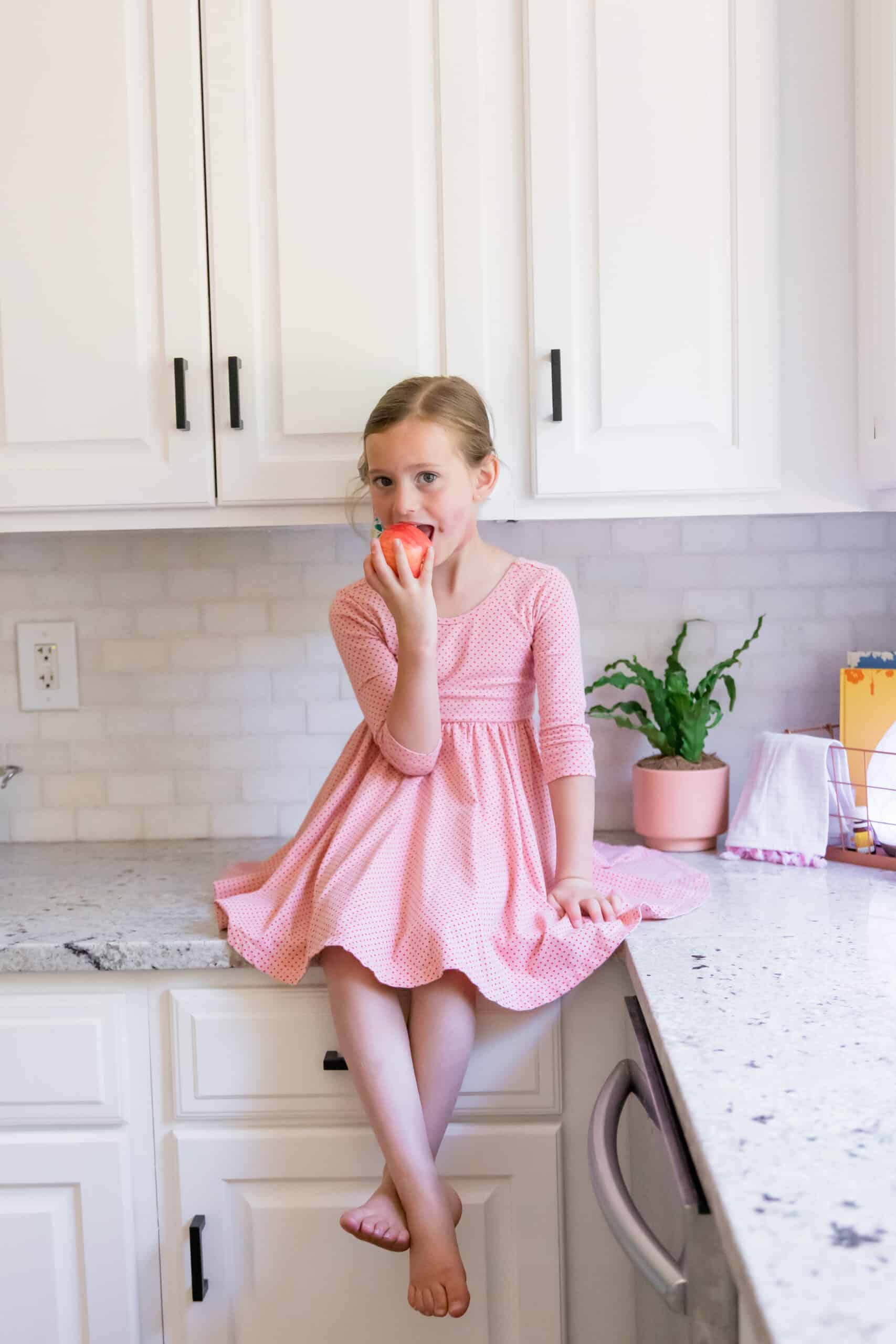 toddler girl eating apple in white kitchen