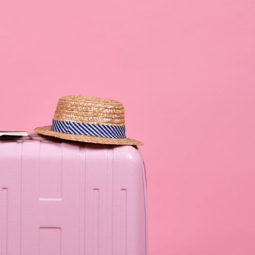 pink suitcase with hat on pink backdrop