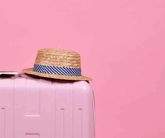 pink suitcase with hat on pink backdrop