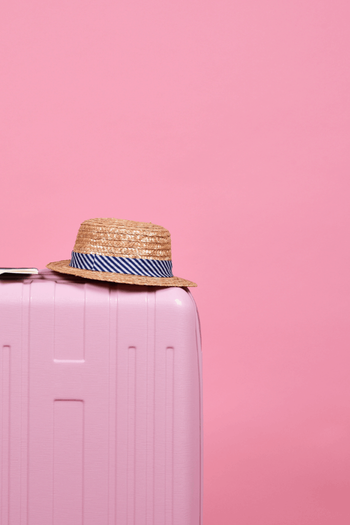 pink suitcase with hat on pink backdrop