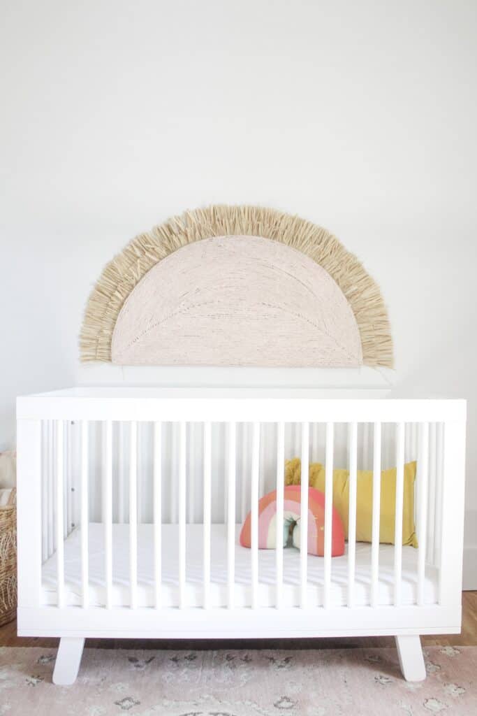 white crib with large wall hanging sunshine over 