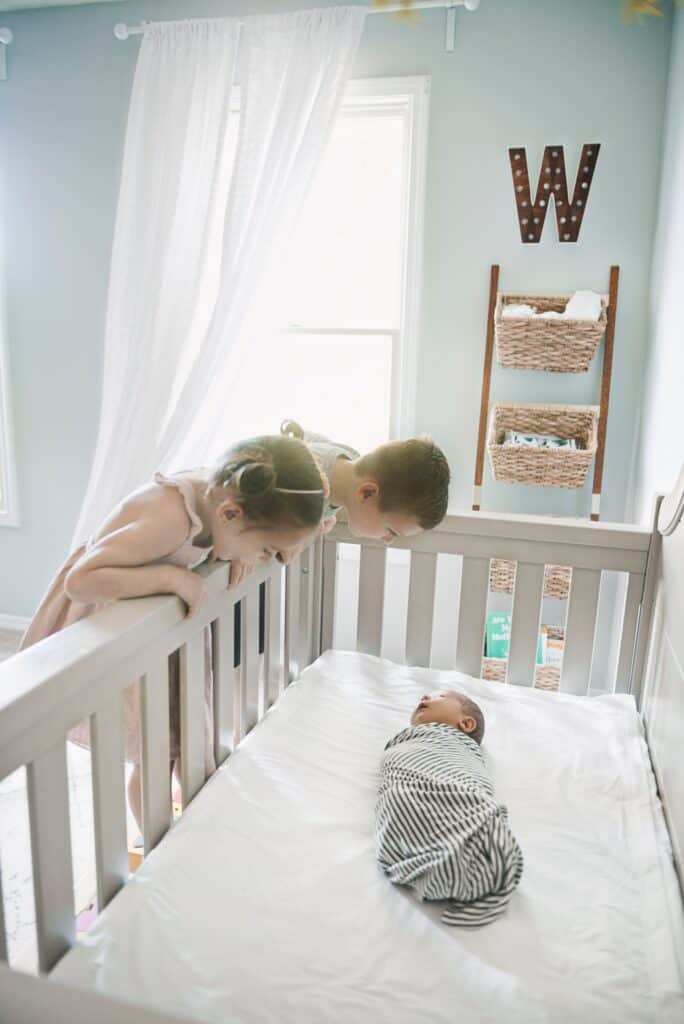 siblings with baby in crib