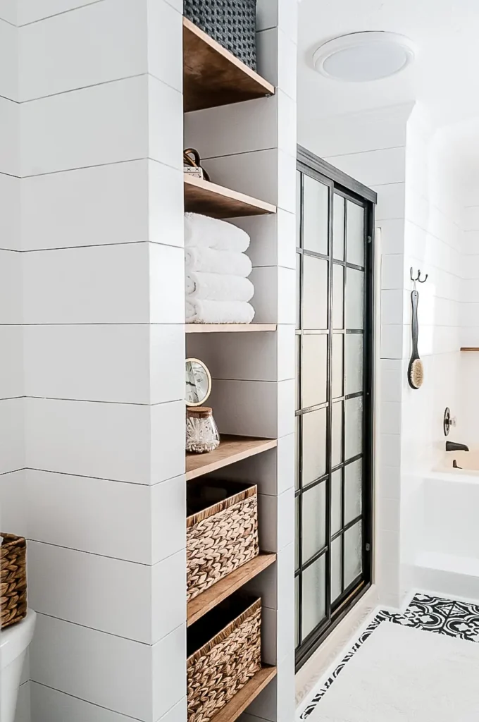 White and black bathroom with built in shelves for towels, baskets, and decorative objects.
