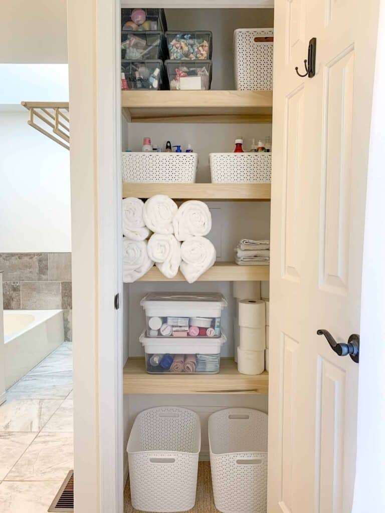 Bathroom linen closet with white baskets and rolled towels.